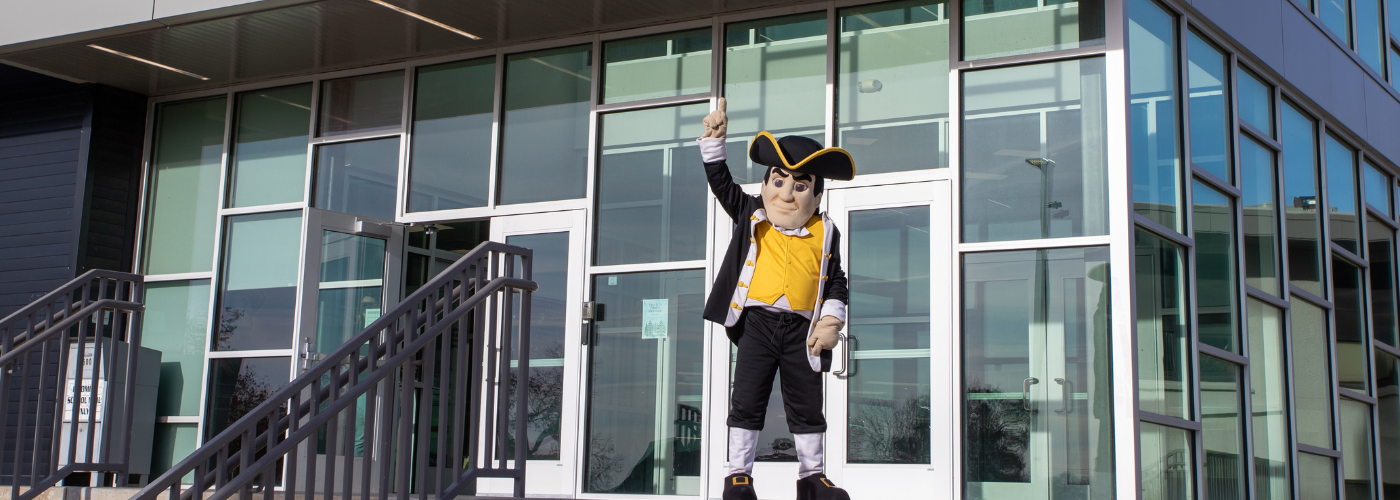 Minuteman Mascot standing outside Charles Page High School, raising his index finger in the air