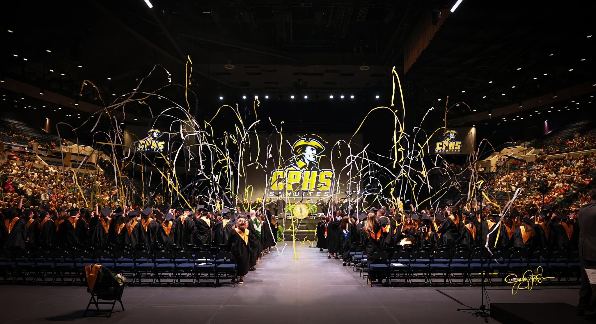 Graduation commencement with CPHS logo on the screen and yellow and white streamers flying in the air.
