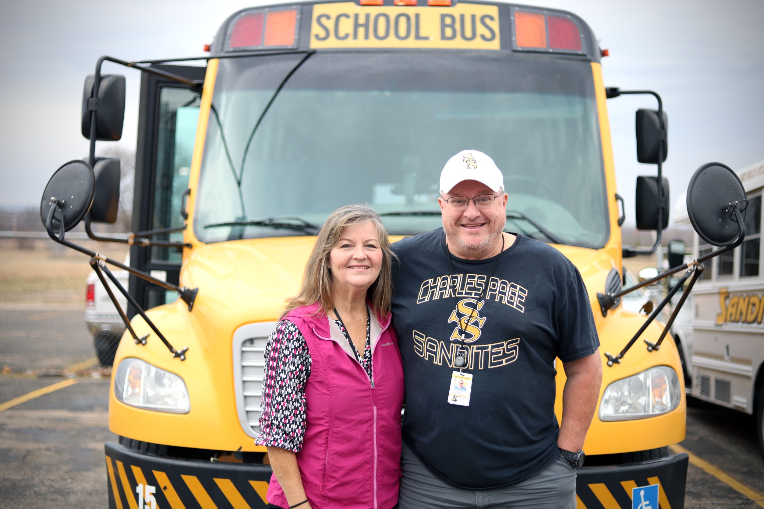 Two Bus Drivers standing and smiling in front of a yellow bus
