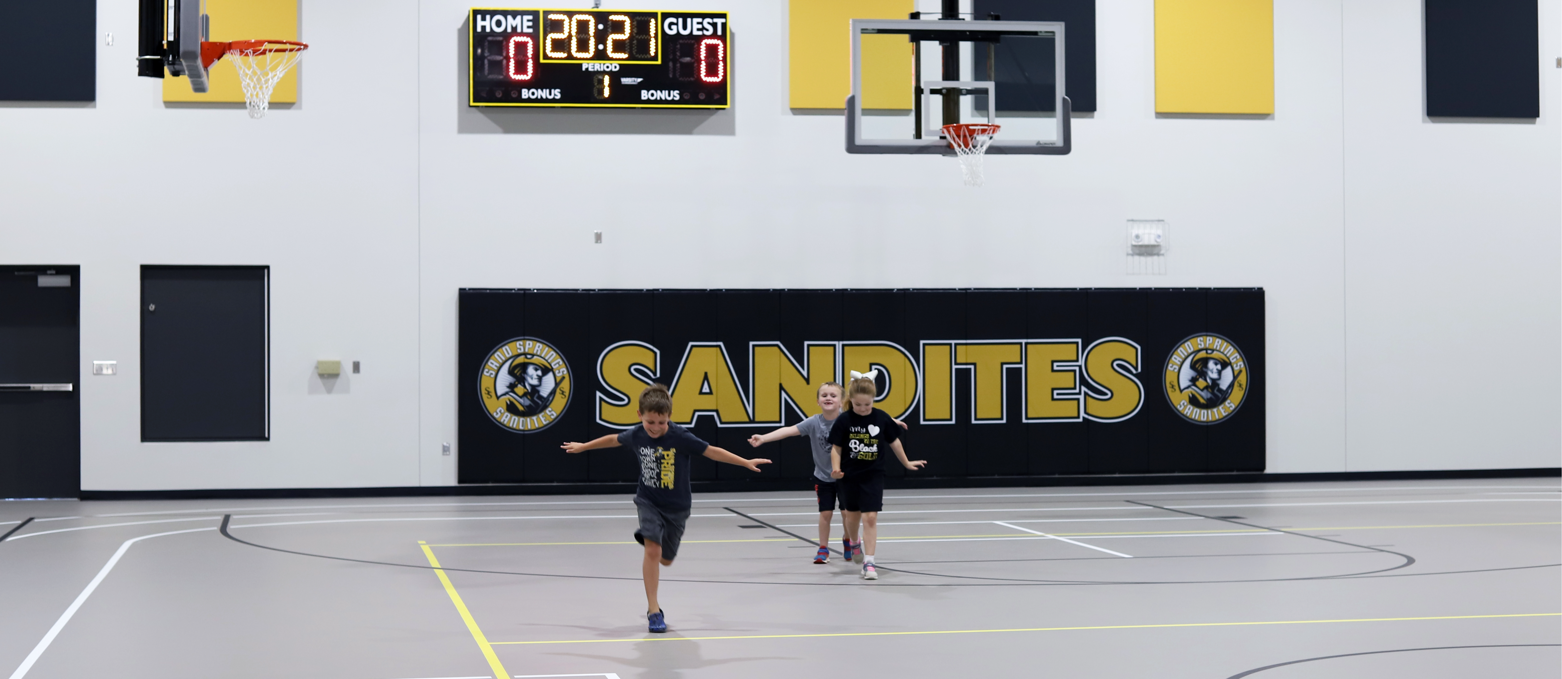 Kids running in a gymnasium with the text "Sandites" on the wall