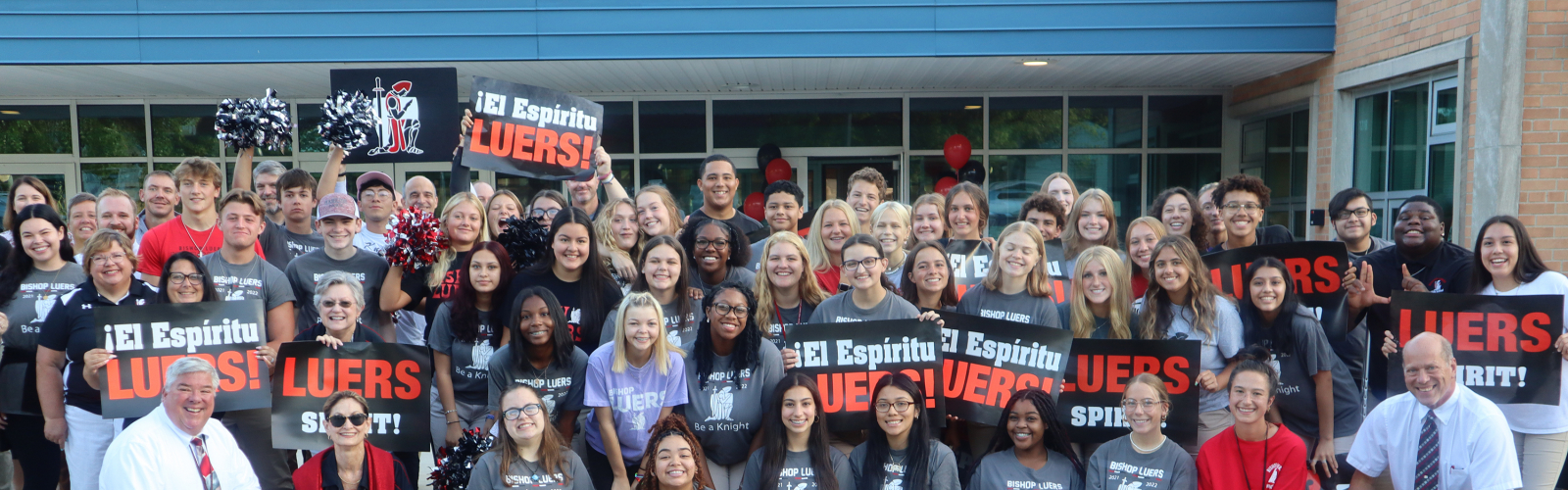 a large group of students smiling and holding "El espíritu Luers!/Luers Spirit!" banners