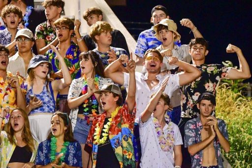 a group of students in Hawaiian shirts cheering and raising their arms