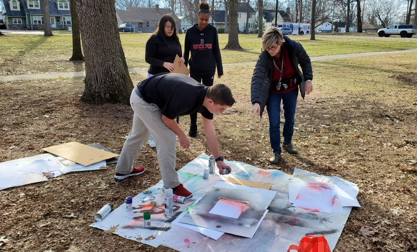students doing spray-paint art outside under the guidance of a teacher