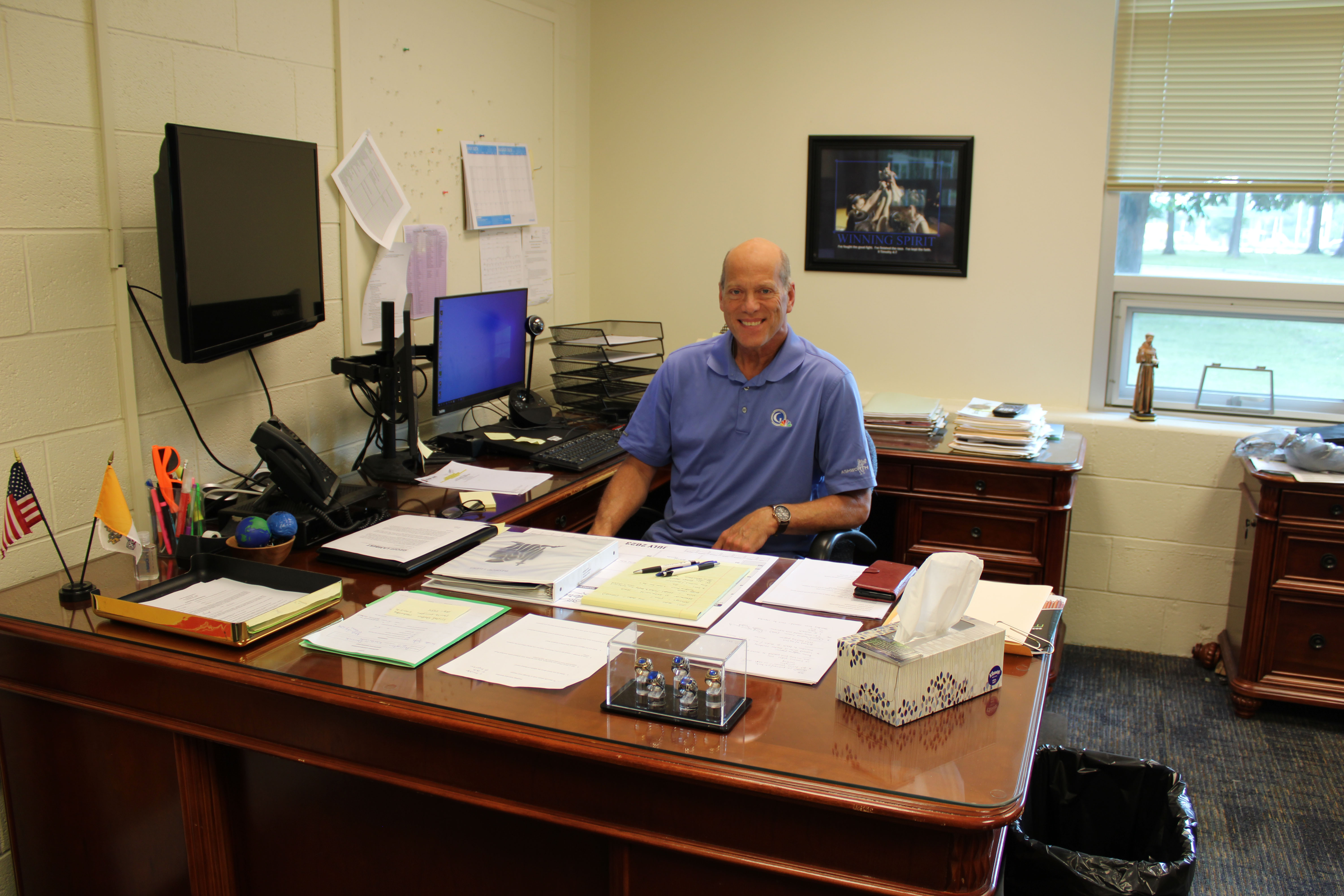 Principal Jim Huth in a suit standing to the right of a faculty member in front of the Bishop Luers logo and smiling