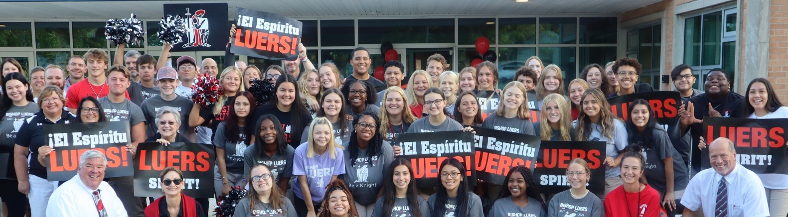 a large group of students smiling and holding "El espíritu Luers!/Luers Spirit!" banners