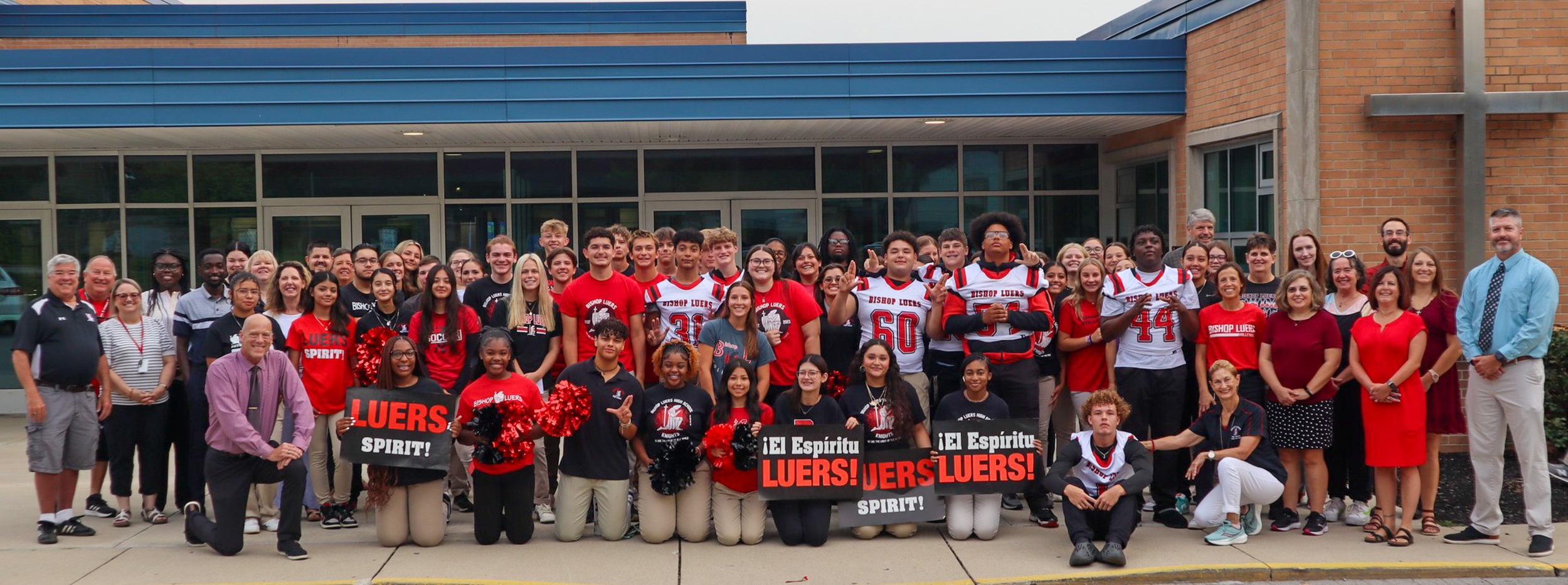 a large group of students smiling and holding "El espíritu Luers!/Luers Spirit!" banners