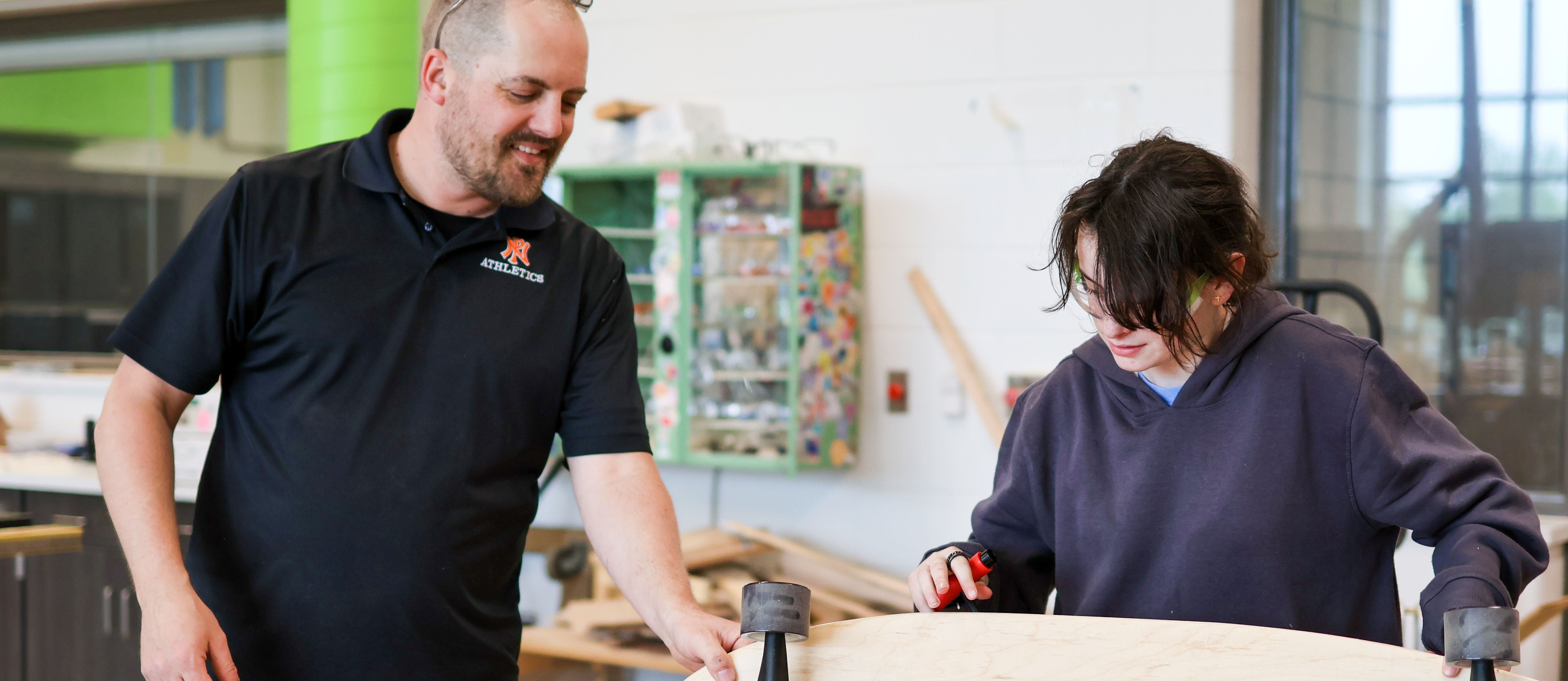 A teacher helps a student with her woodshop project