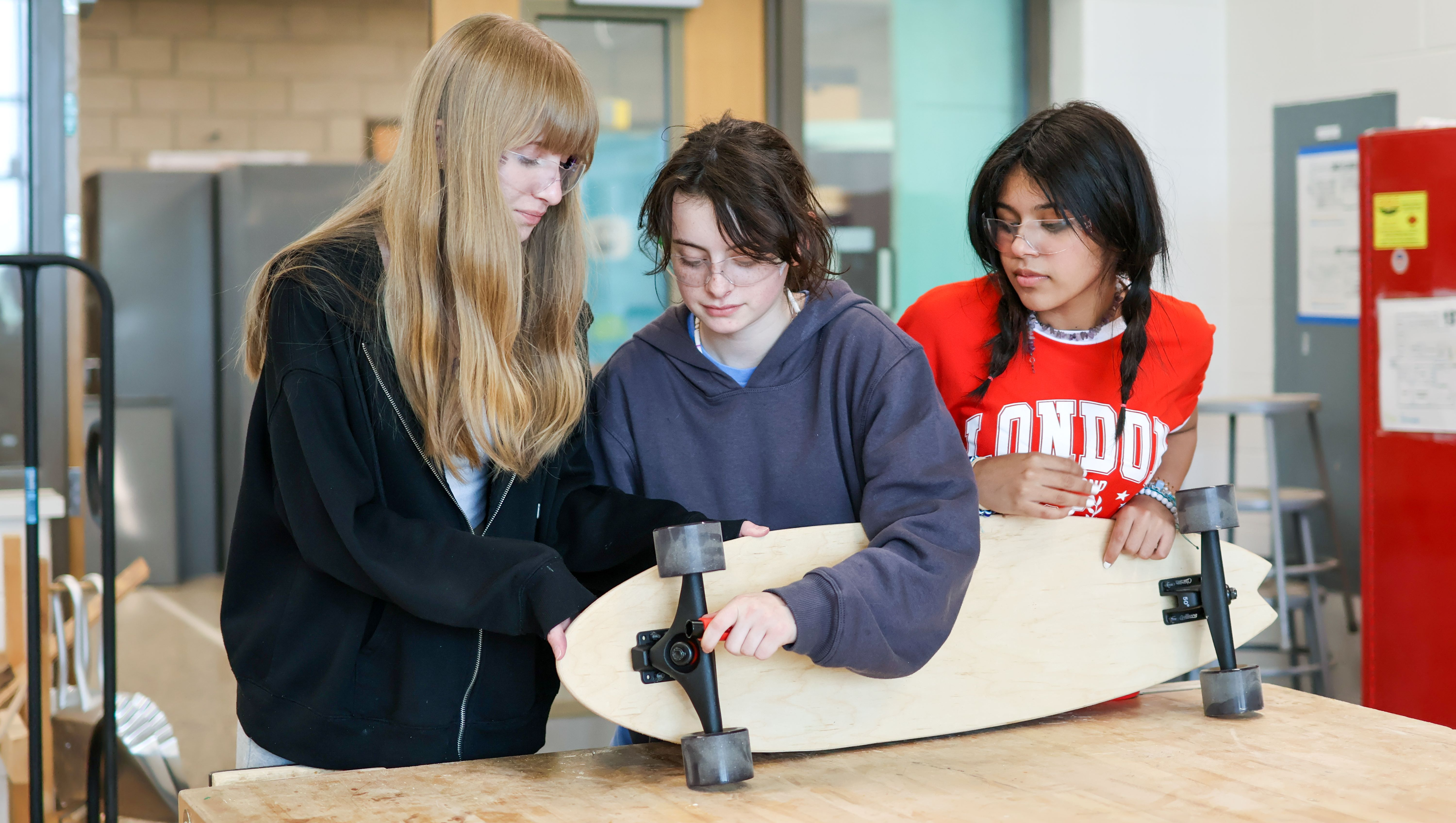 three students work on a woodworking project