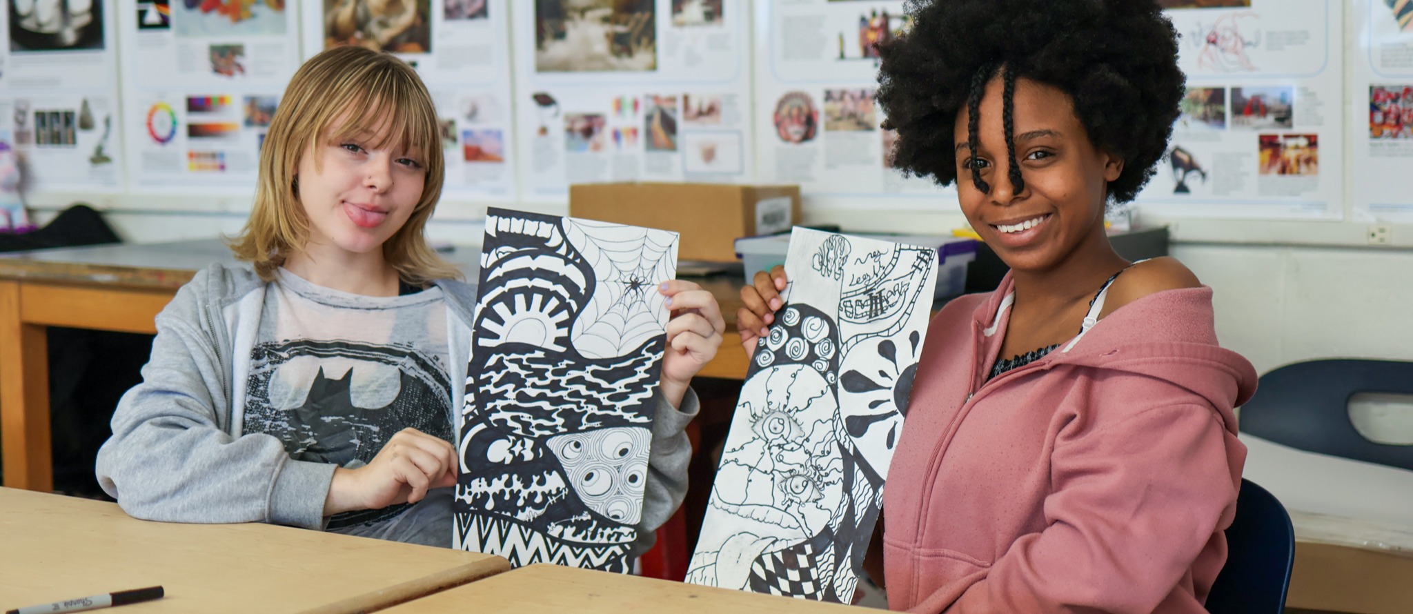 two students smile for a photo holding up artwork