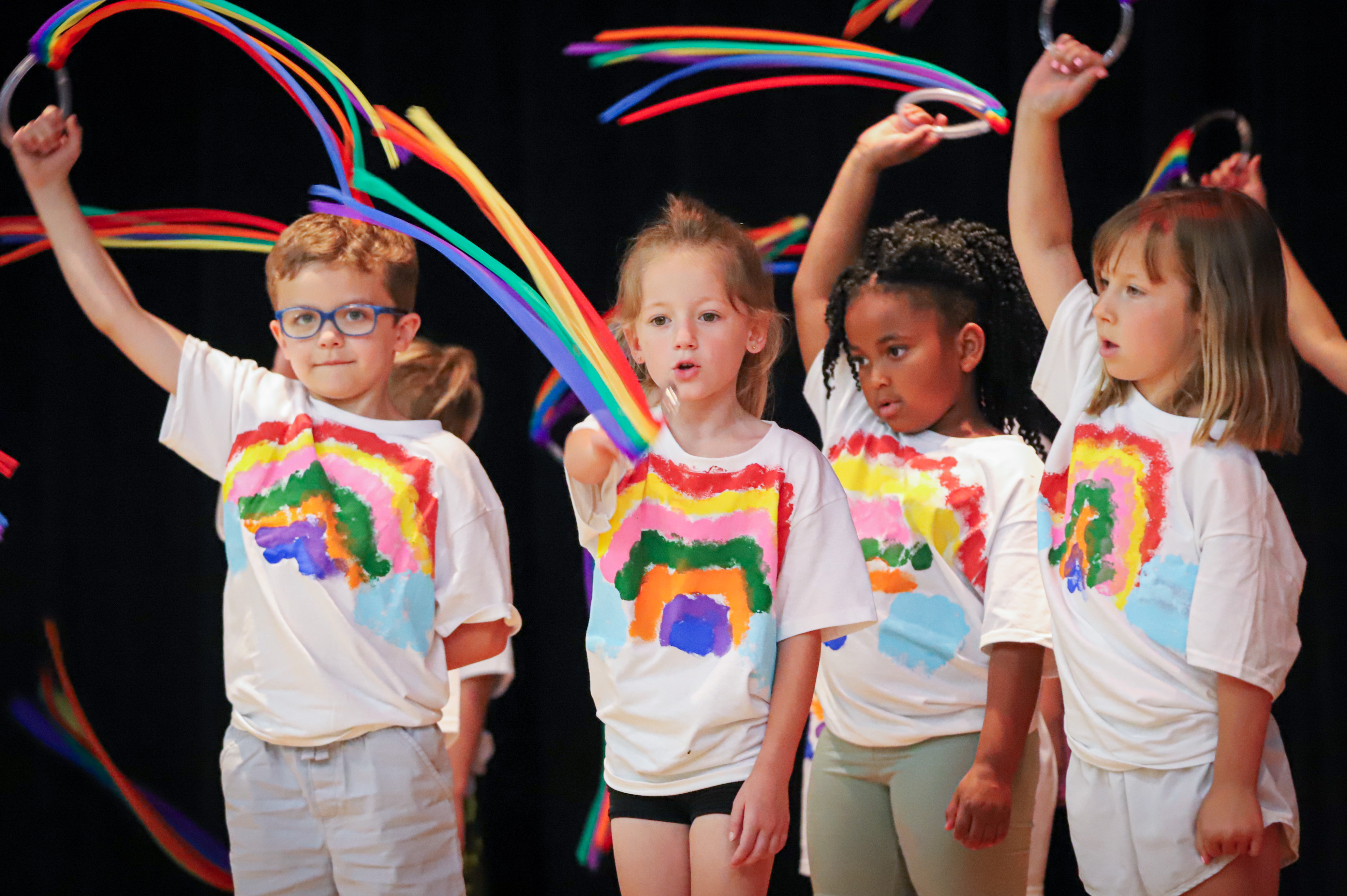 Kindergarten students in handmade rainbow shirts waving multicolored streamers