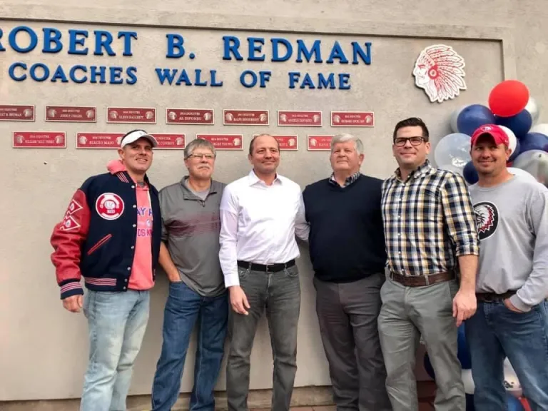 6 males in front of redman coaches hall of fame wall