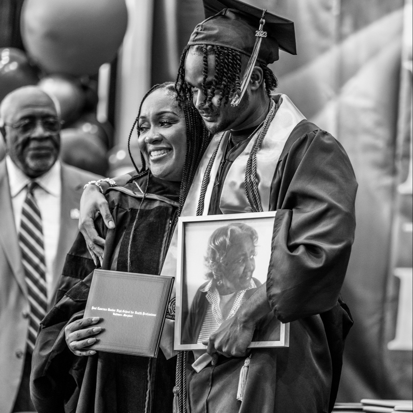 Young man poses with mother and picture of grandmother at Dunbar high school graduation