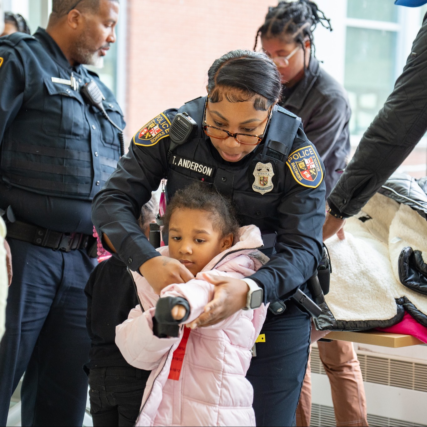 School police officer assists elementary school student with putting on her coat.