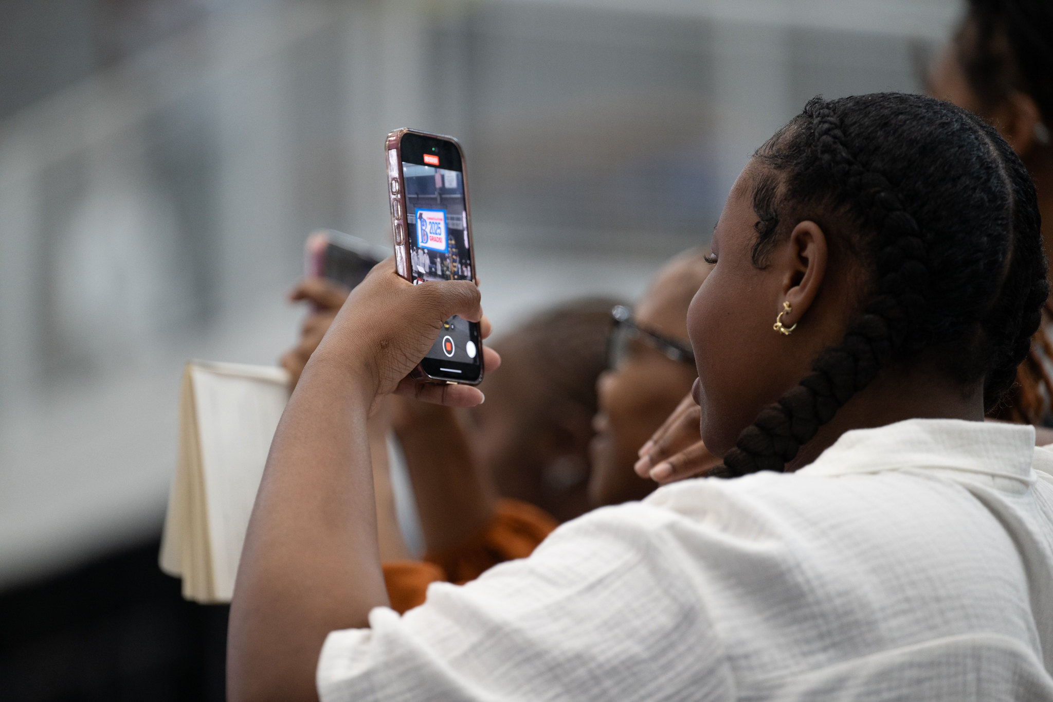 Young woman holds up a phone at a graduation ceremony. 