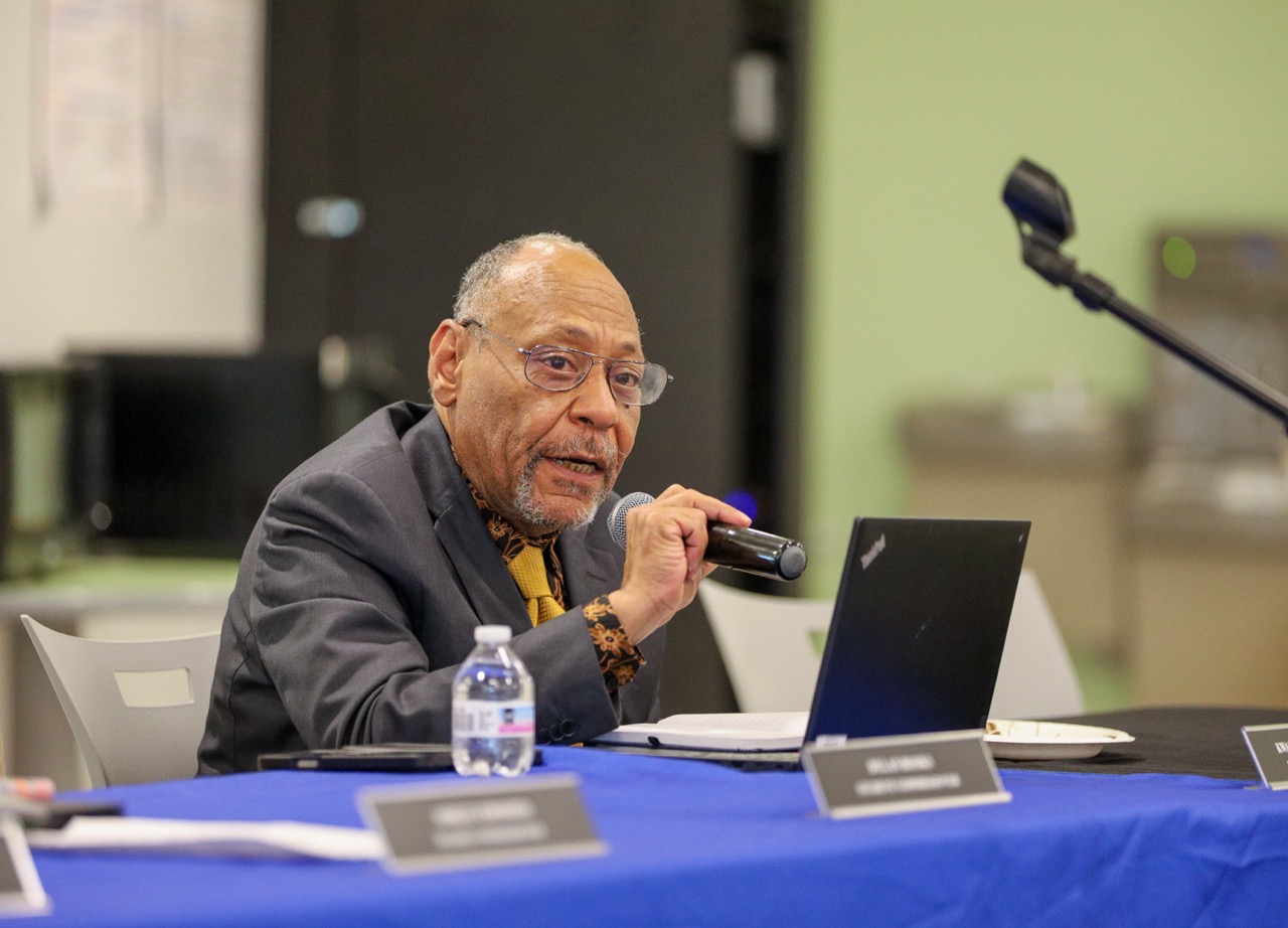 Board member speak into the microphone as he addresses the crowd at a hearing. 