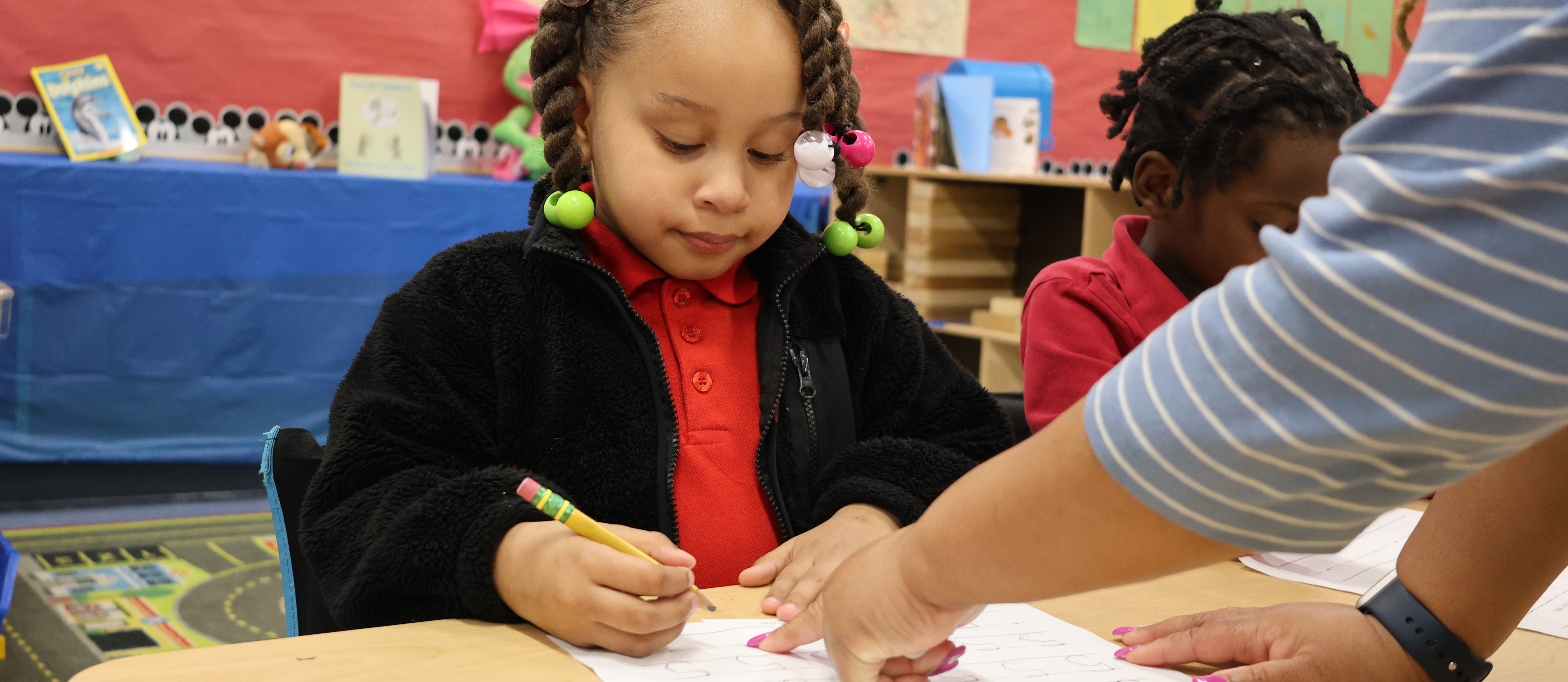 Pre-K student sitting at desk receiving instruction from teacher