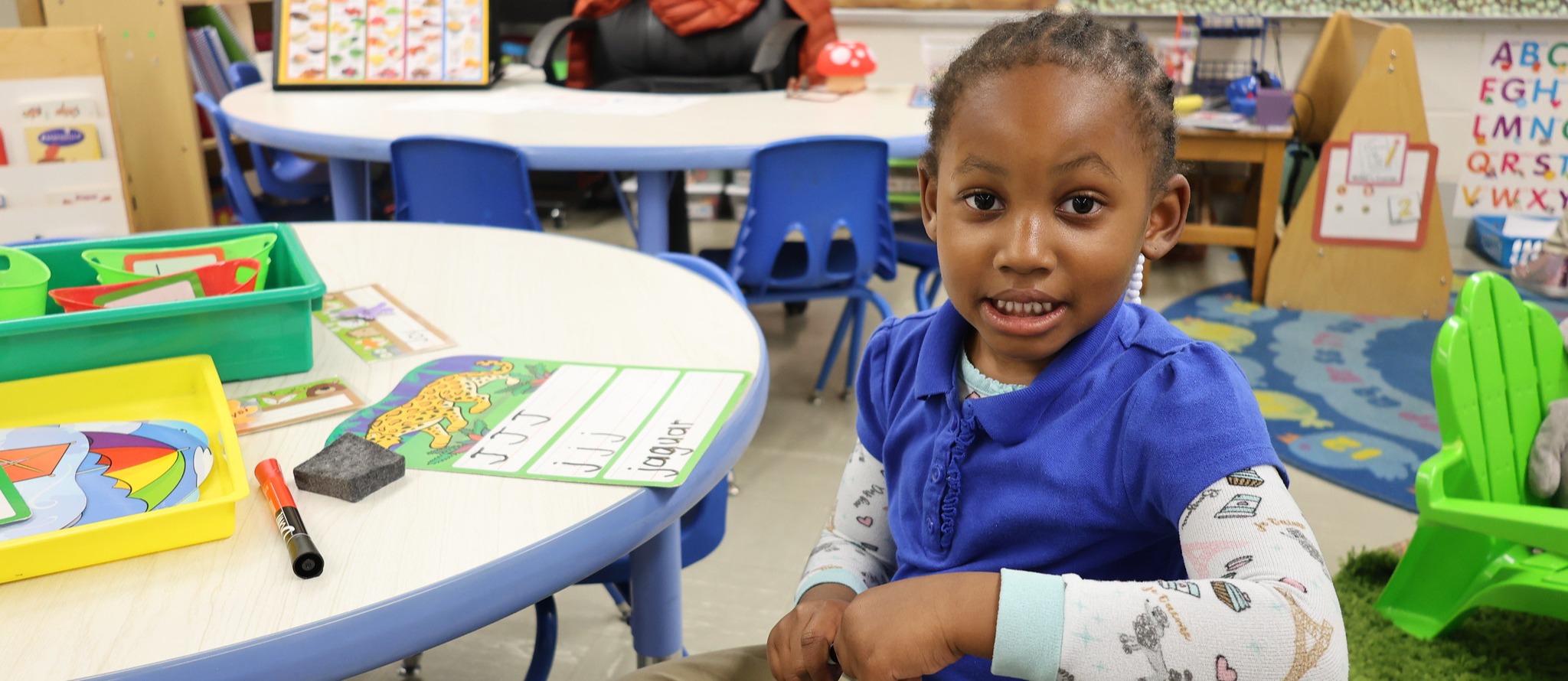 Pre-k student sitting at their desk smiling at the camera