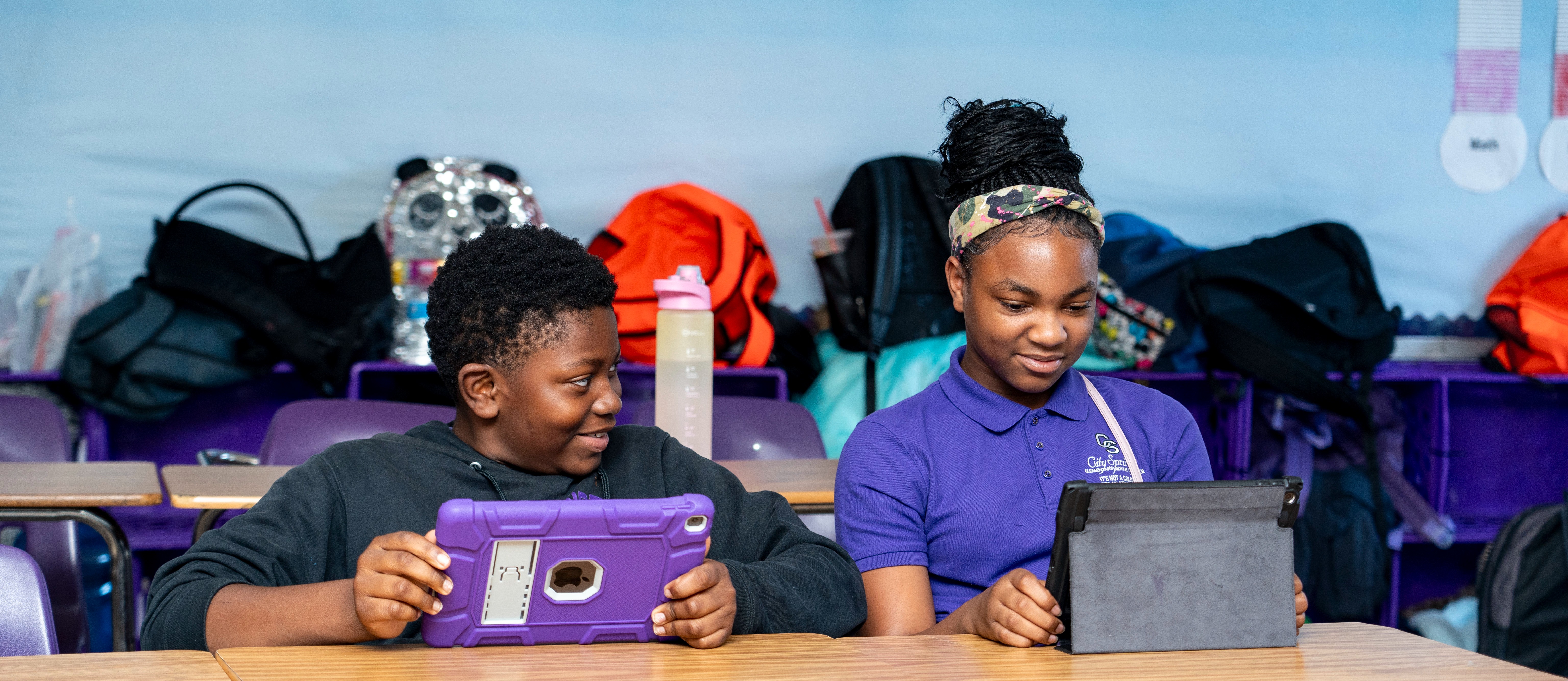 Two students smiling at their desk with tablets in their hands