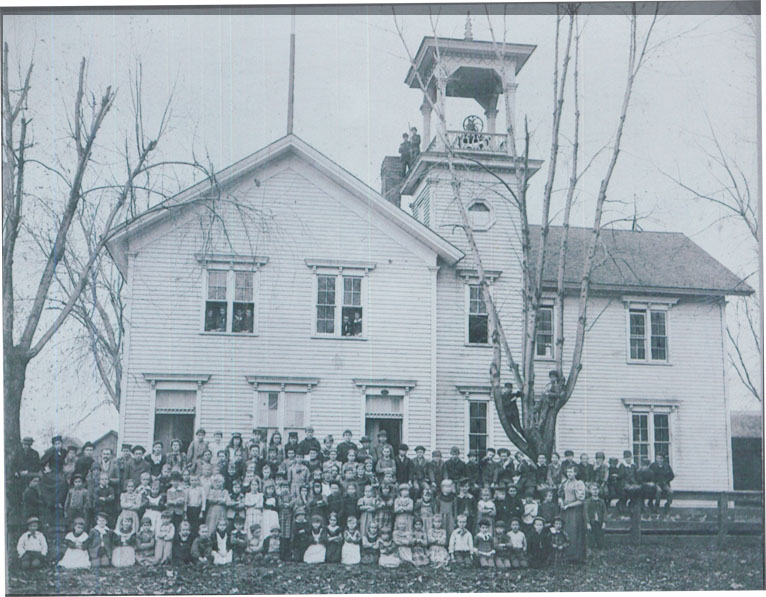 A black and white photo of all the students standing in front of the school's building.