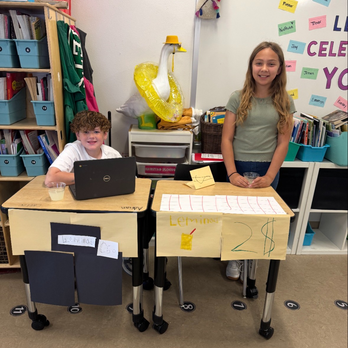 two students with lemonade stand signs on desks