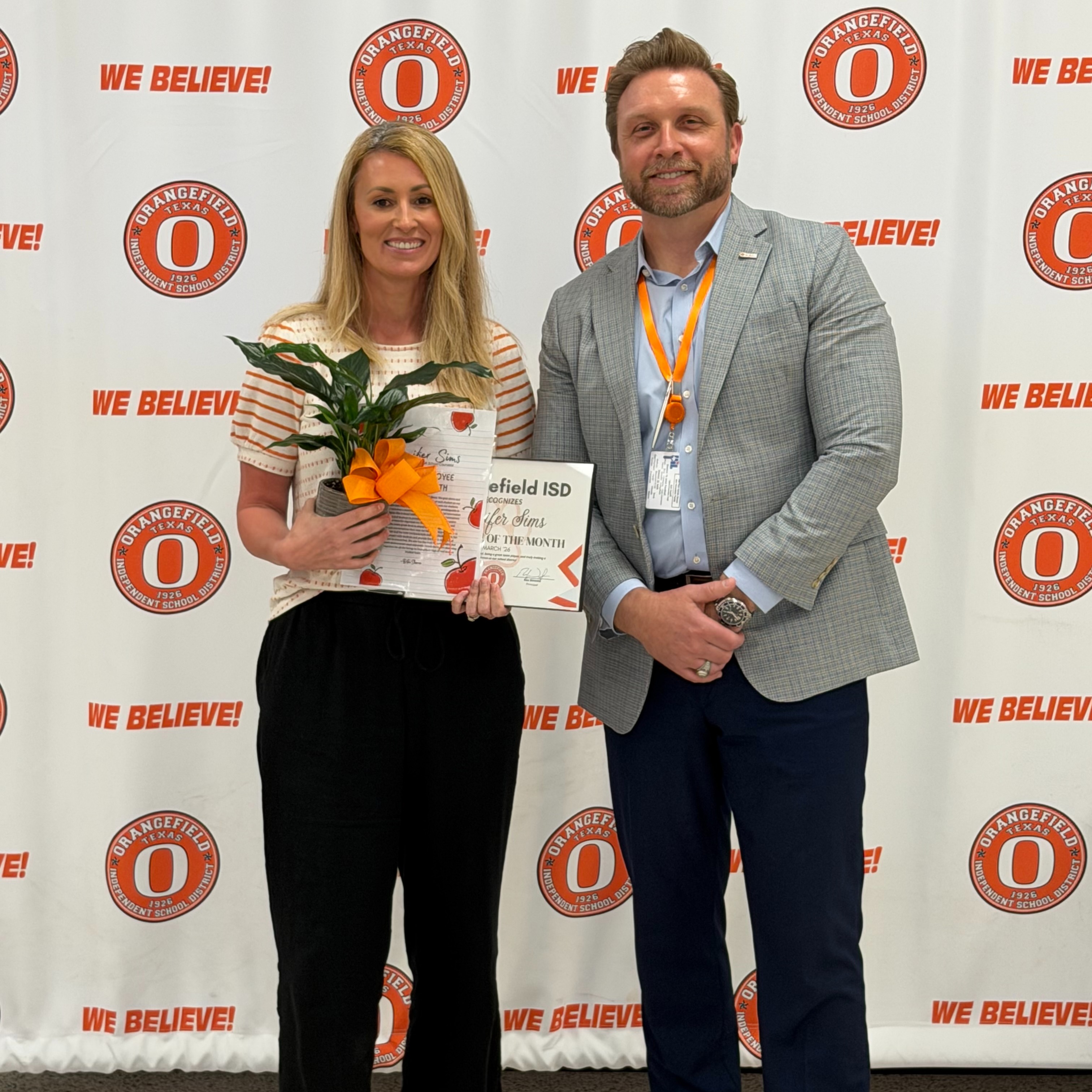 Woman in black pants and a white shirt holding a plaque standing next to a man in a gray suit.