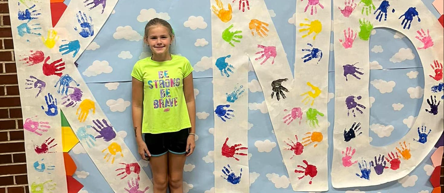 Lincoln 4th grade student standing in front of bulletin board reading "Be the I in Kind"