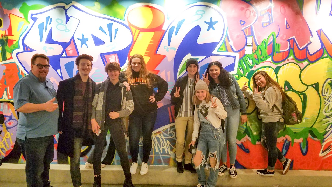 students standing in front of a graffiti-style mural and grinning