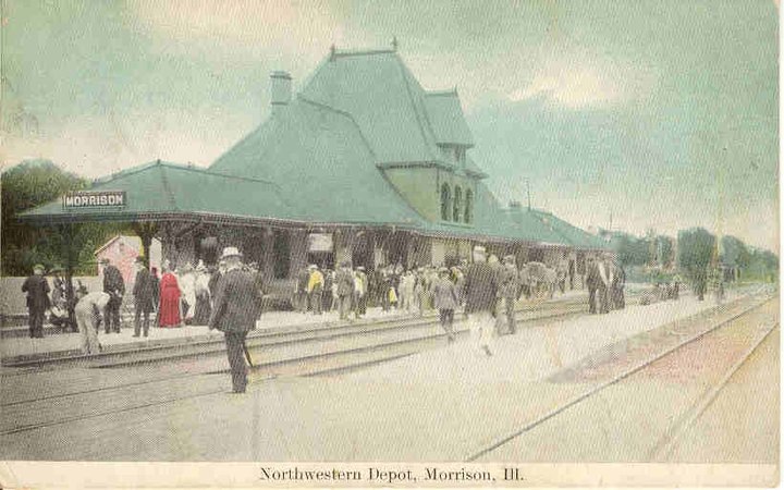 photo of depot building that has a tall green roof with people milling about out front