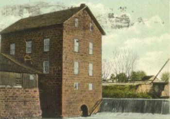 old photo of the exterior of the mill with waterfall next to the multi-story building