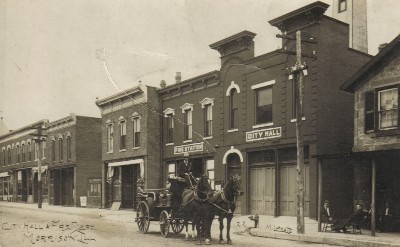 black and white photo of downtown with a horse drawn carriage on the street