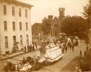 sepia toned photo of building with parade float pulled by horses going by