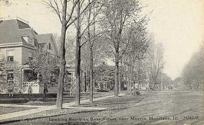 black and white photo of street lined with trees and houses nestled behind them