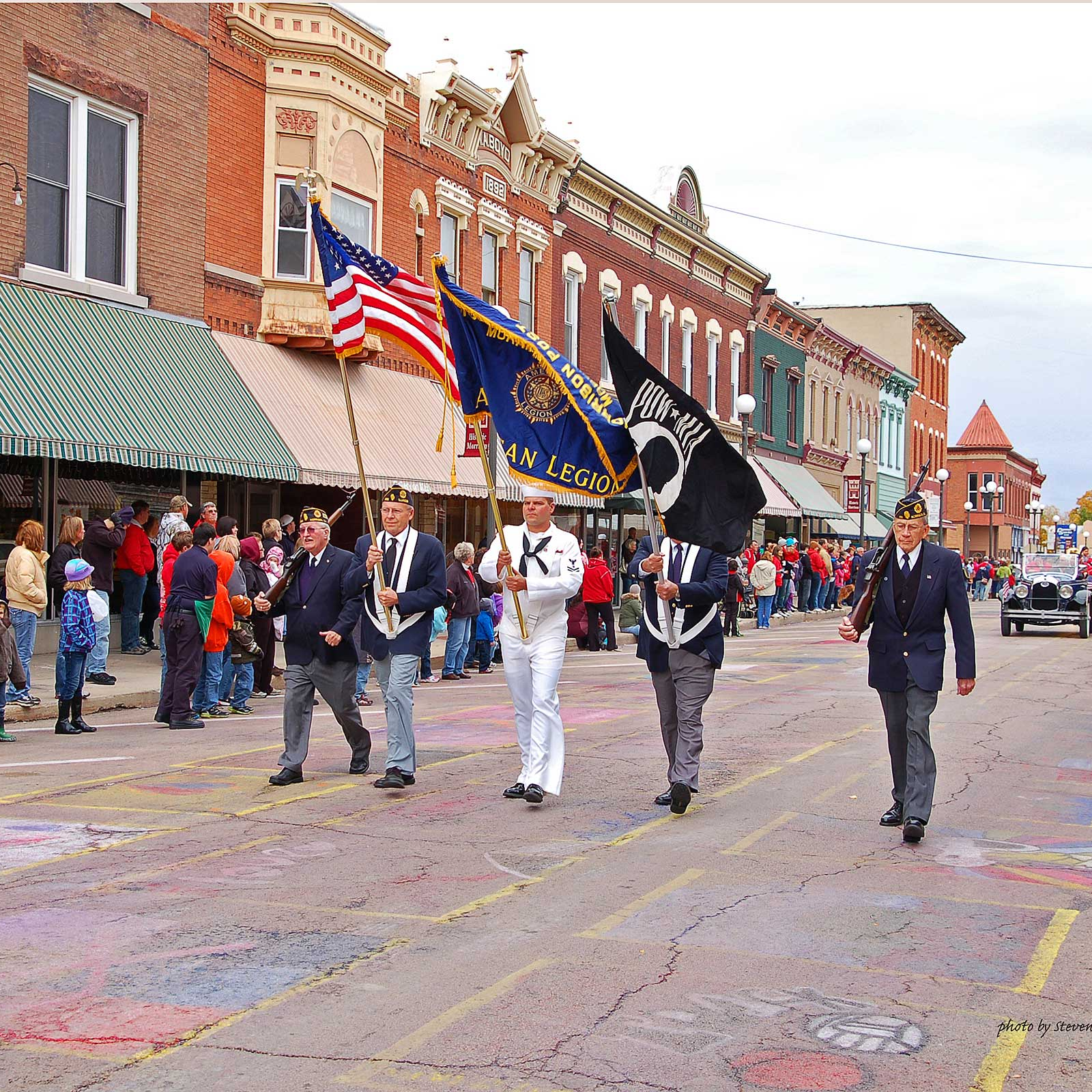 veterans march down main street carrying flags and leading a parade