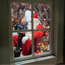 a kid sitting on santa's lap as viewed from the outside of a window