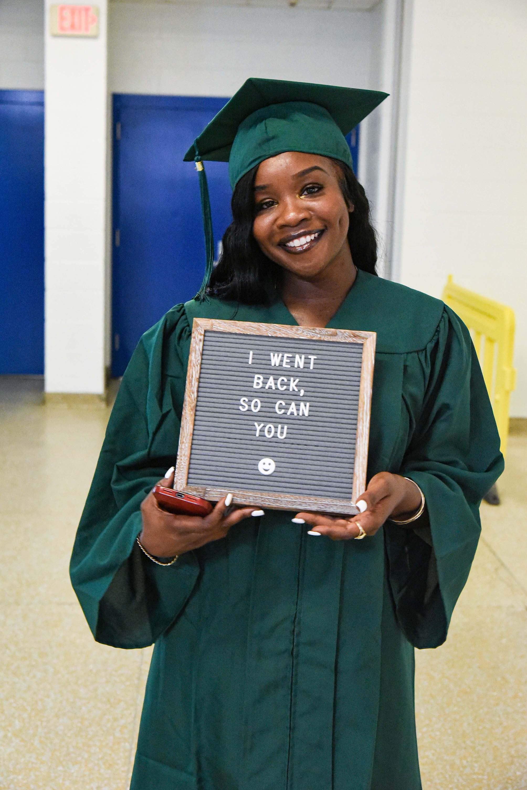 graduate with sign that reads "i went back, so can you"