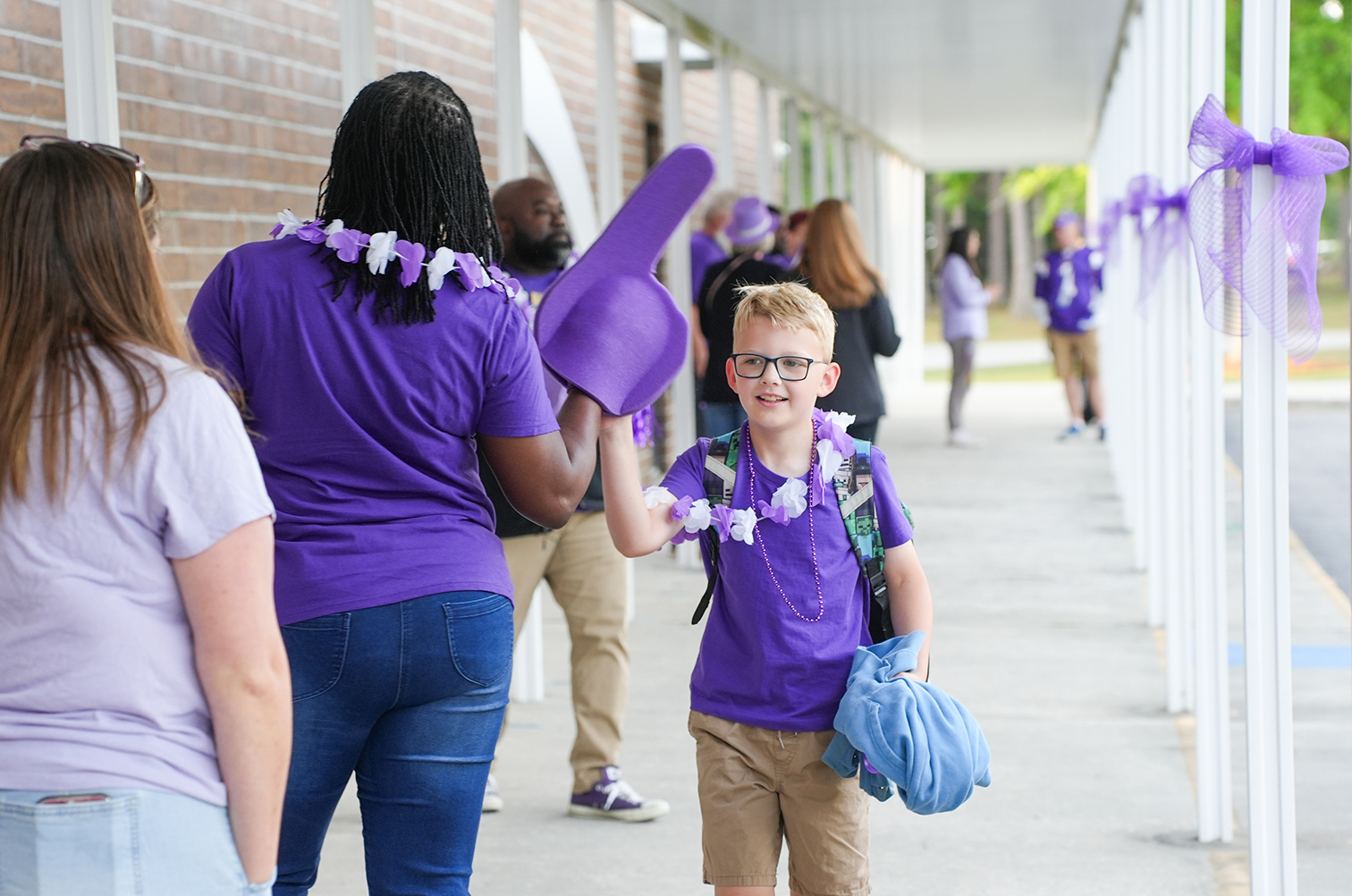 A group of people, including adults and children, wear purple attire and leis outside a building.