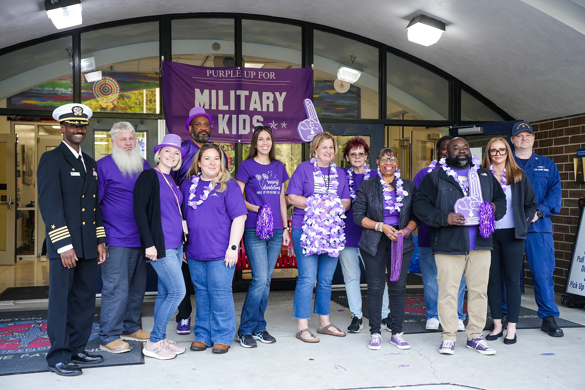 Group of people in purple shirts pose in front of a building with a purple banner above them.