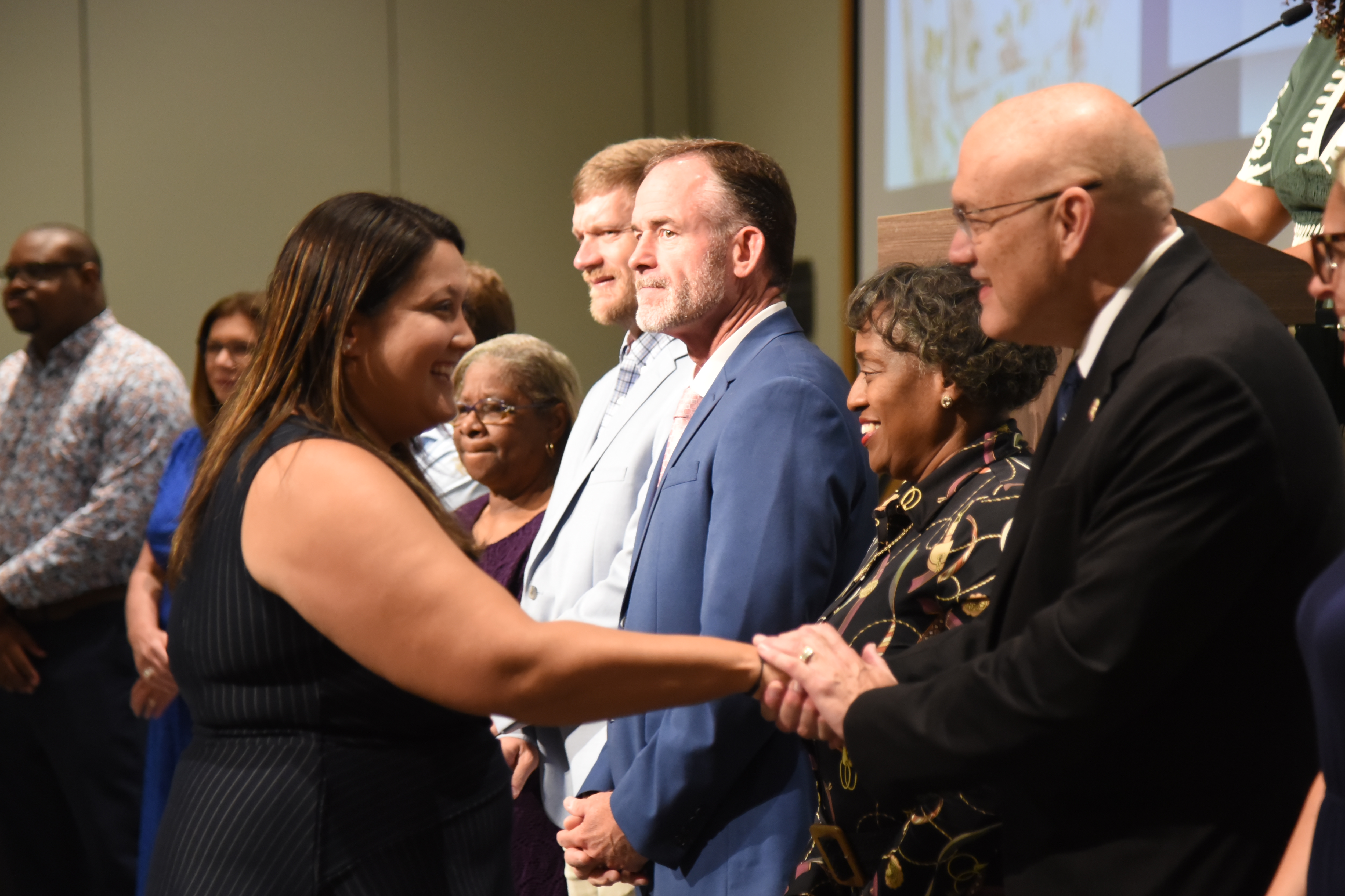 Group of people, including two adults shaking hands, stand indoors, possibly at a ceremony.