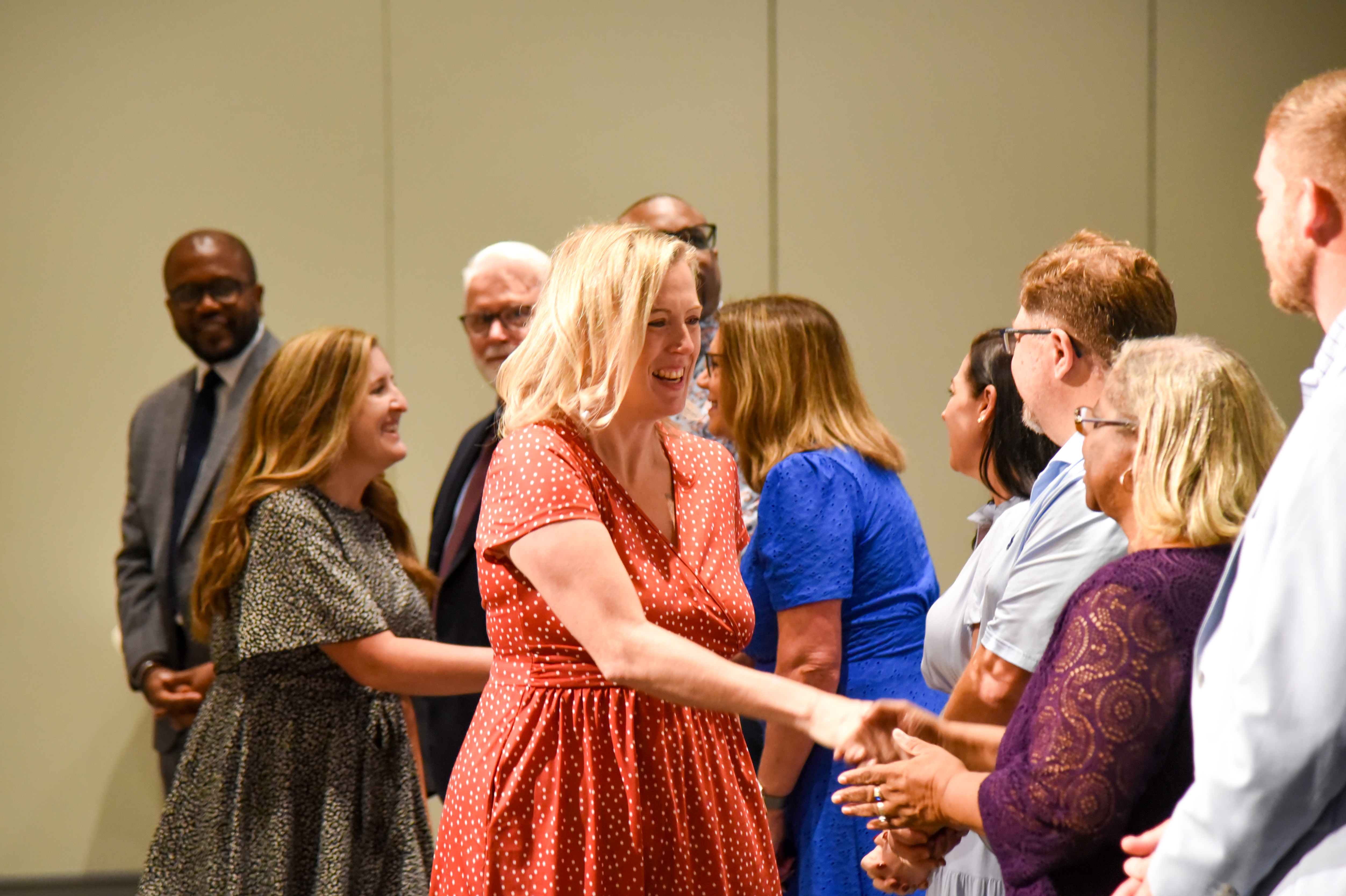 A group of people in formal and casual attire stand and shake hands in a conference room.