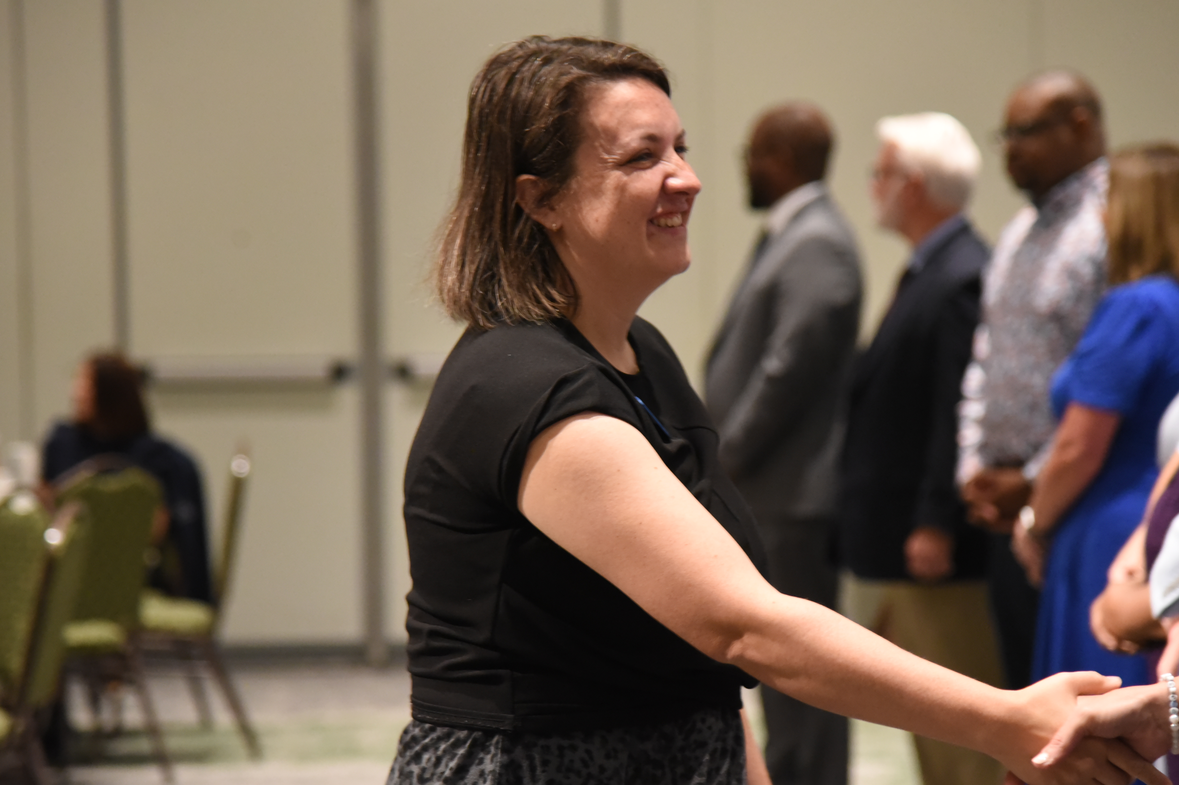 A woman in a black shirt smiles and shakes hands with a person in front of others standing.