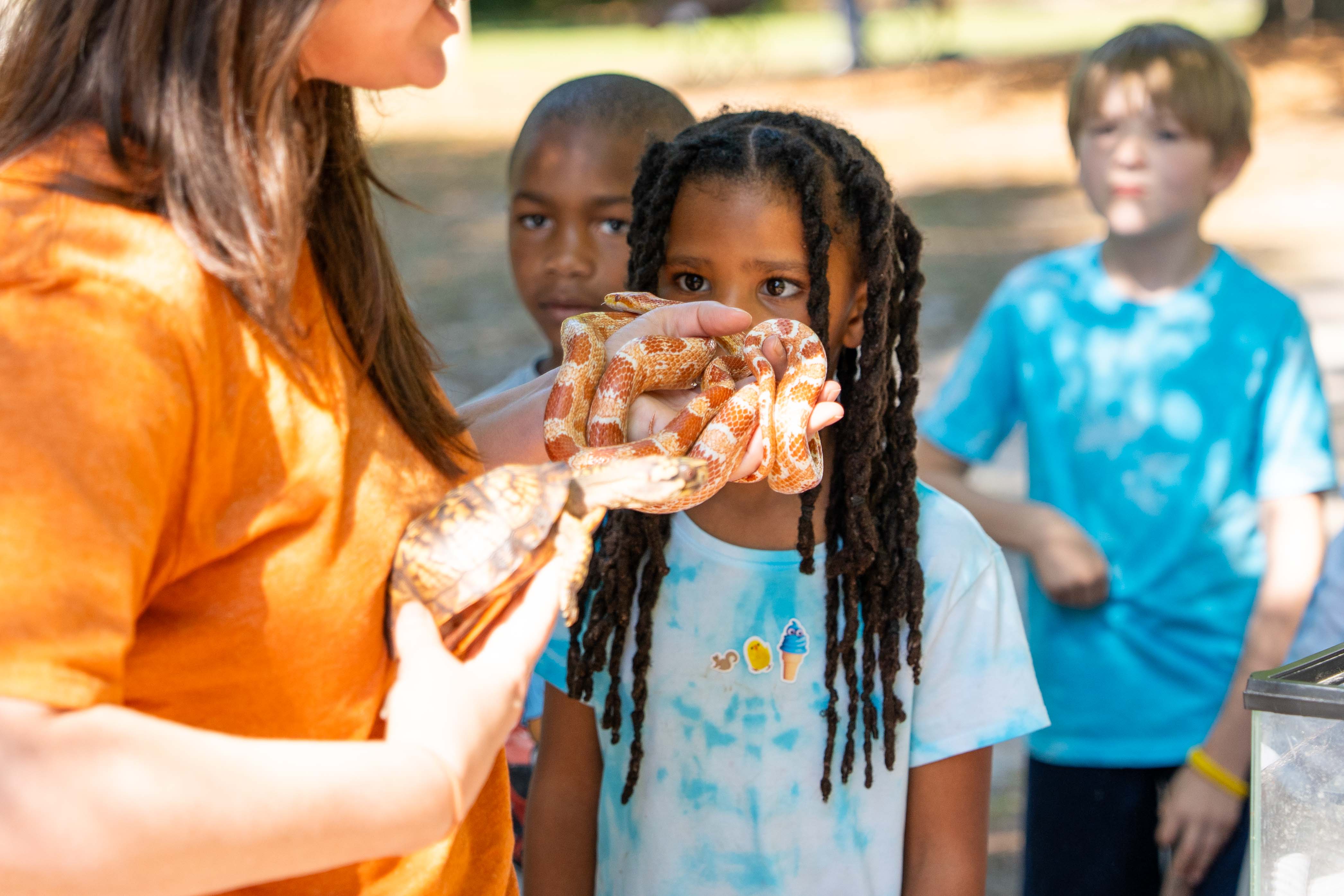 A woman holds a snake while a girl looks on. Another girl and boy stand behind them.