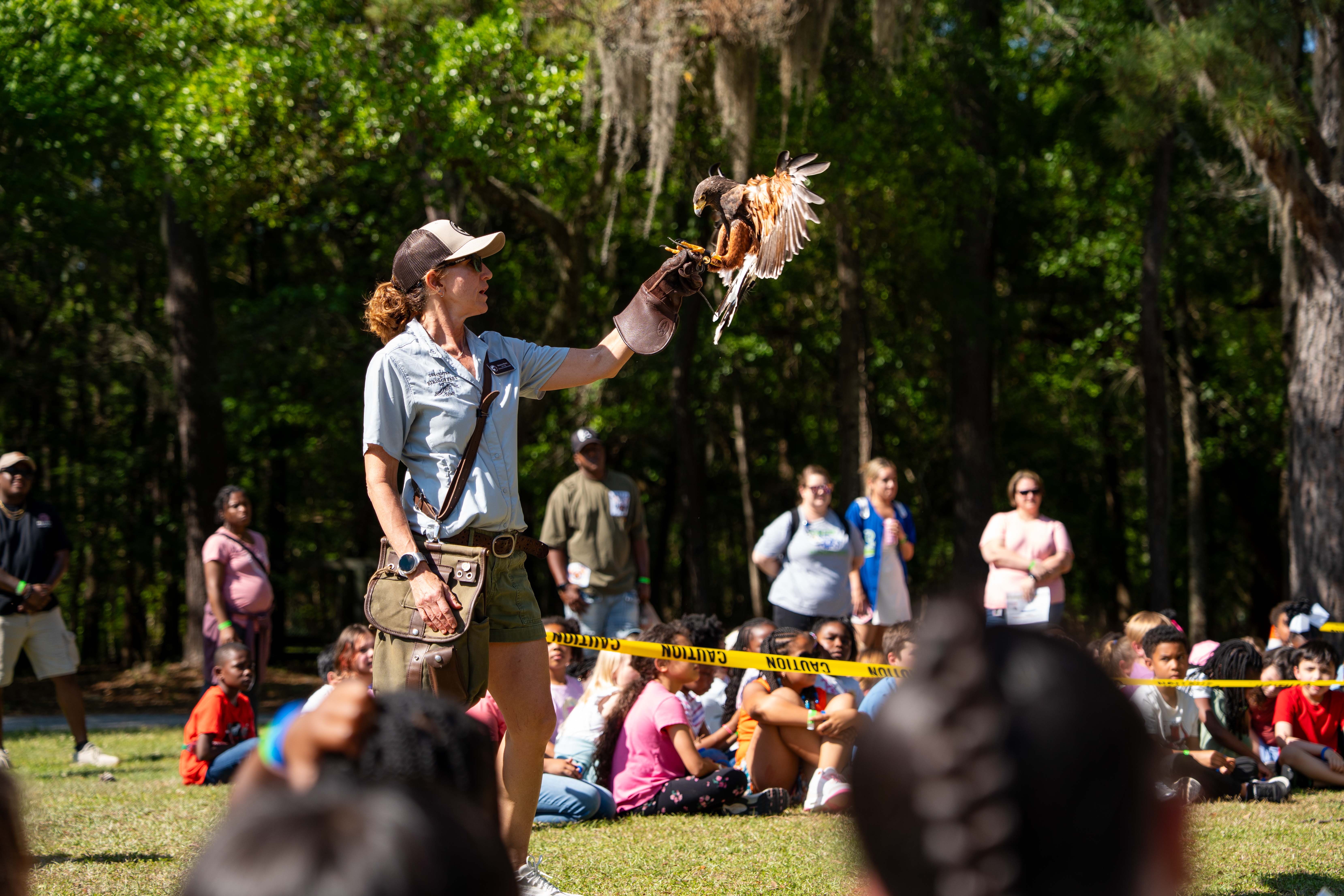 A person in a hat holds a bird while people sit in a circle on grass.