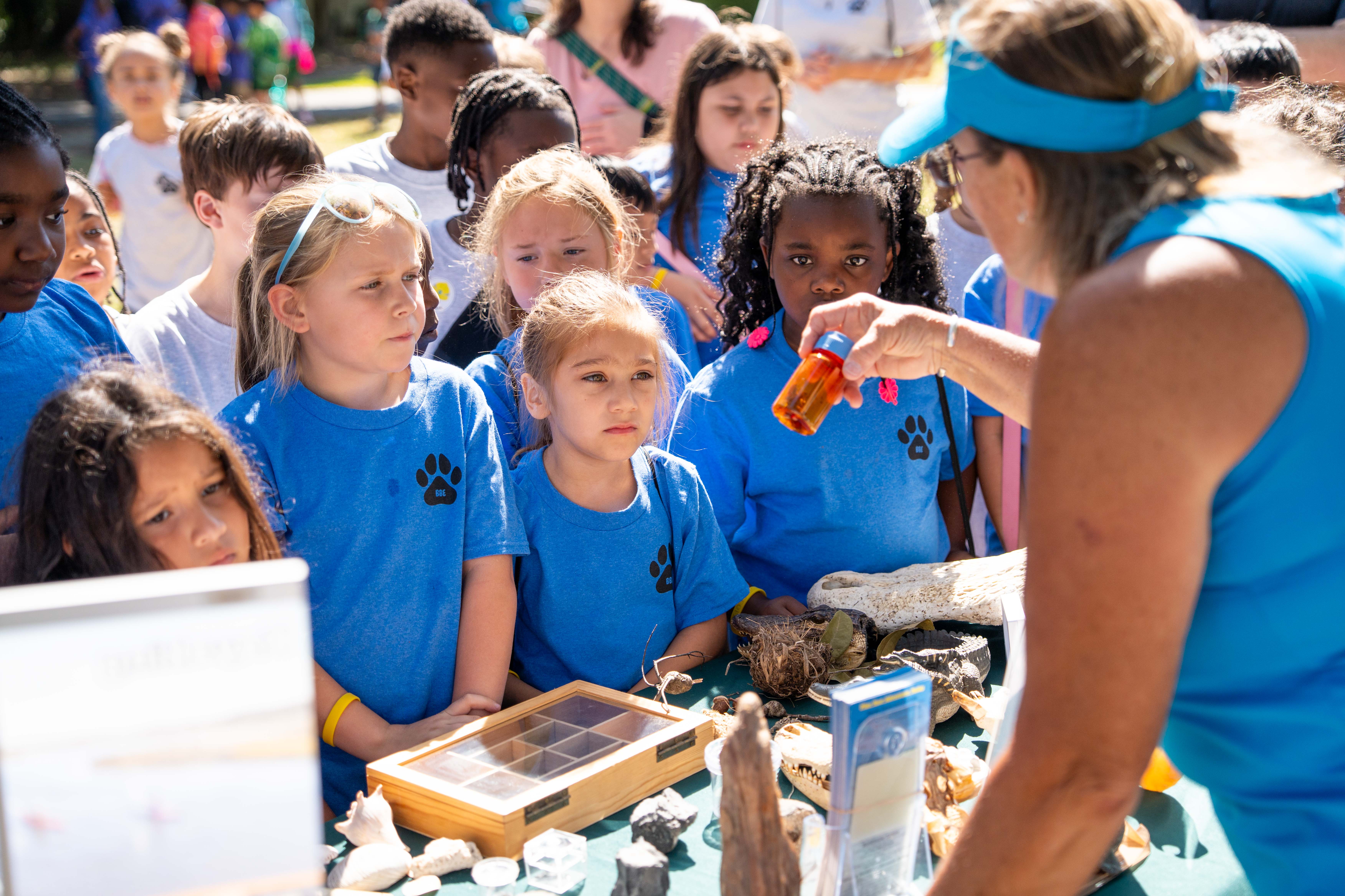 Woman in blue shirt holds up a shell to a group of children in matching shirts.