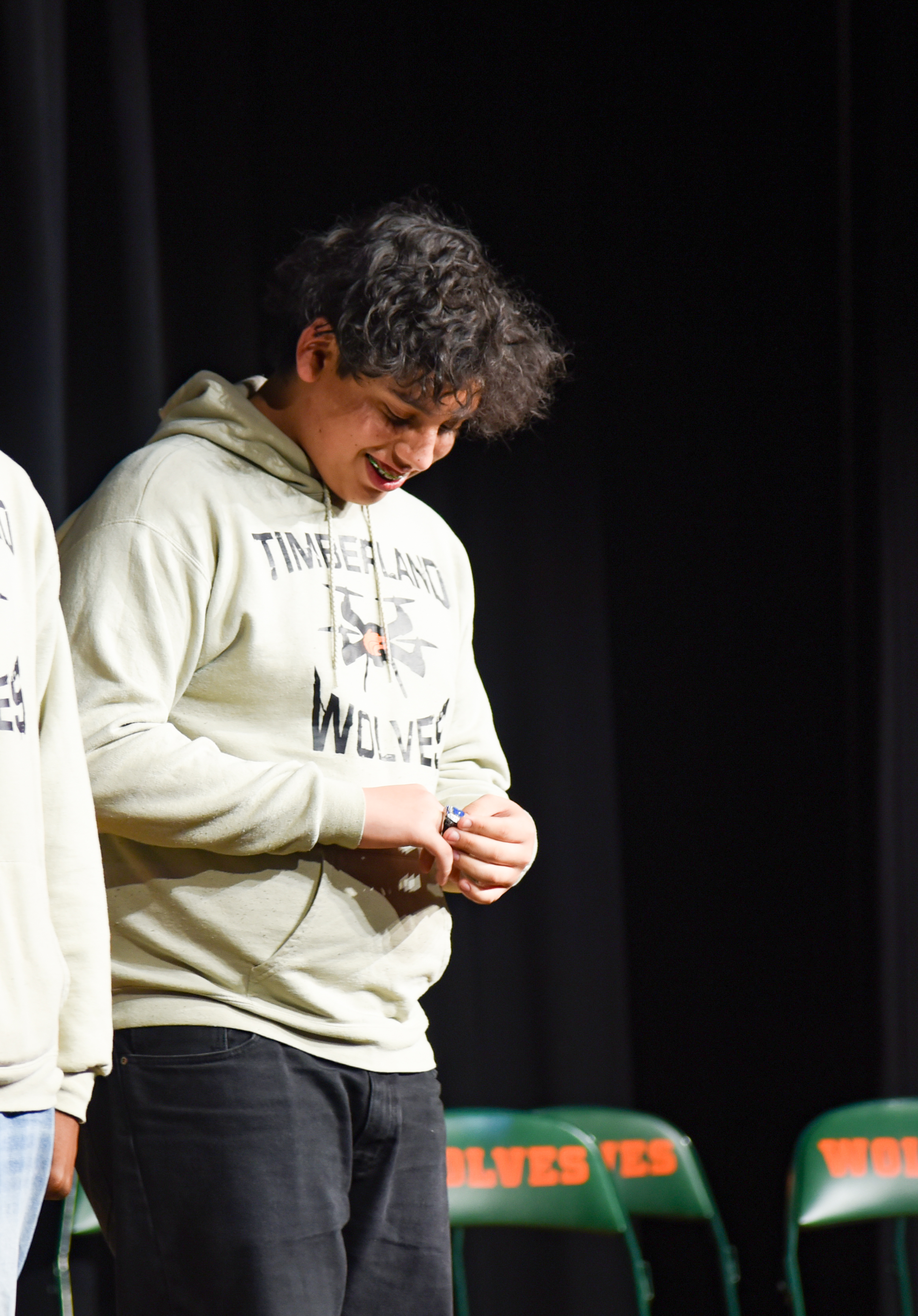 Person wearing Timberland hoodie with a smile, standing on a stage in front of green chairs.