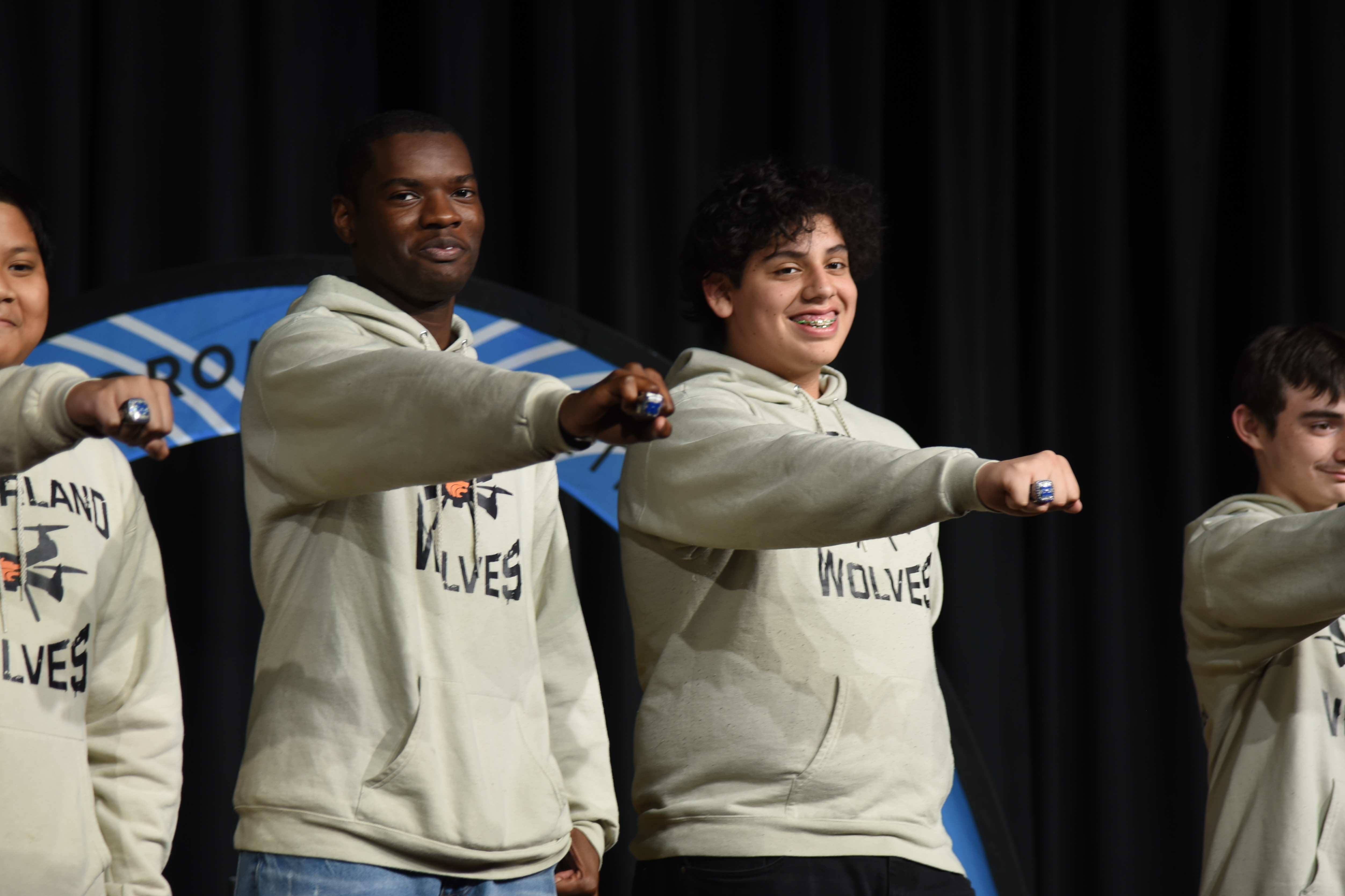 Four young adults in light-colored hoodies, two smiling, gesture with their hands in a studio.