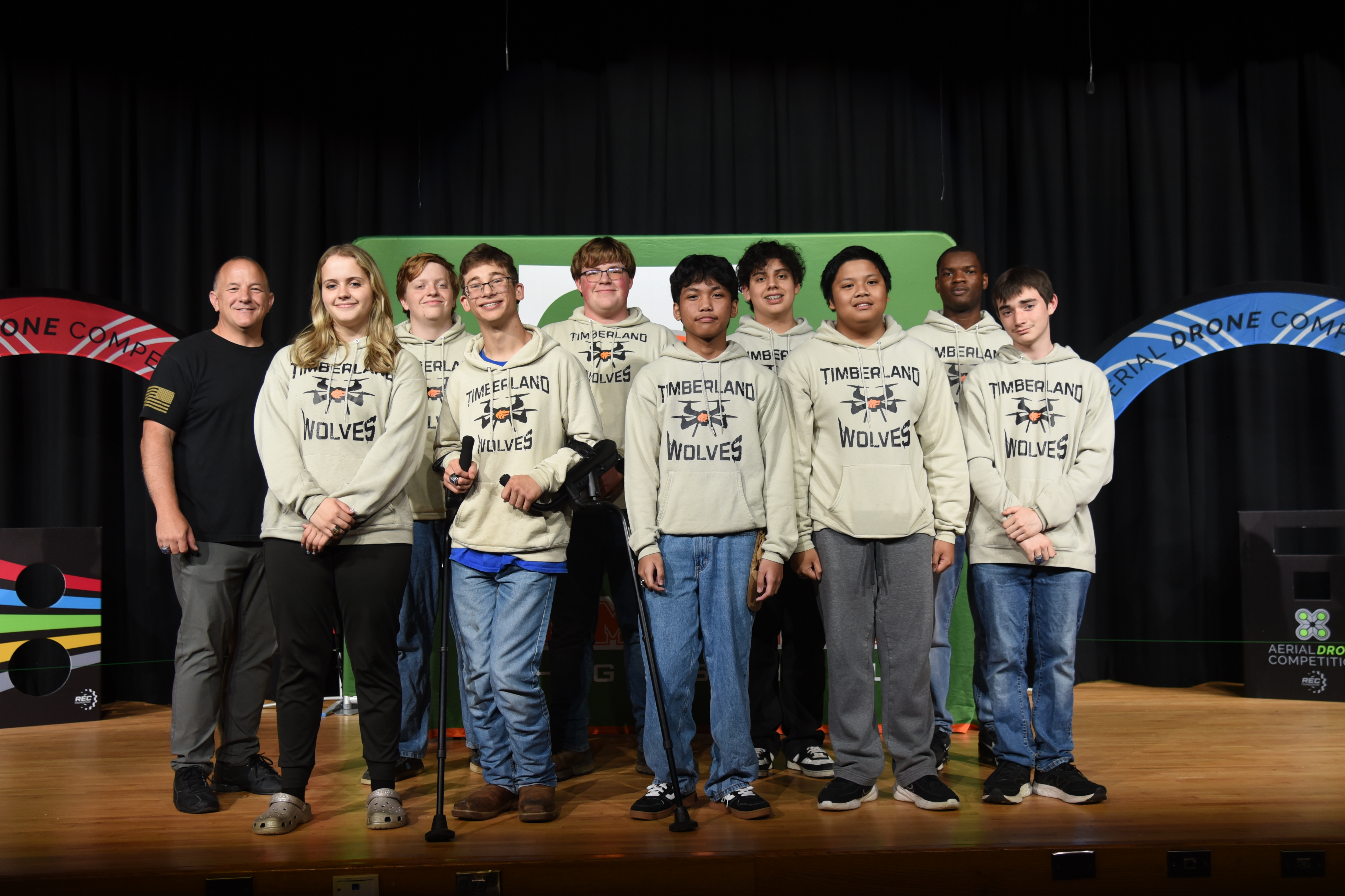 A group of young people, all wearing white sweatshirts, standing on a stage with a colorful backdrop.