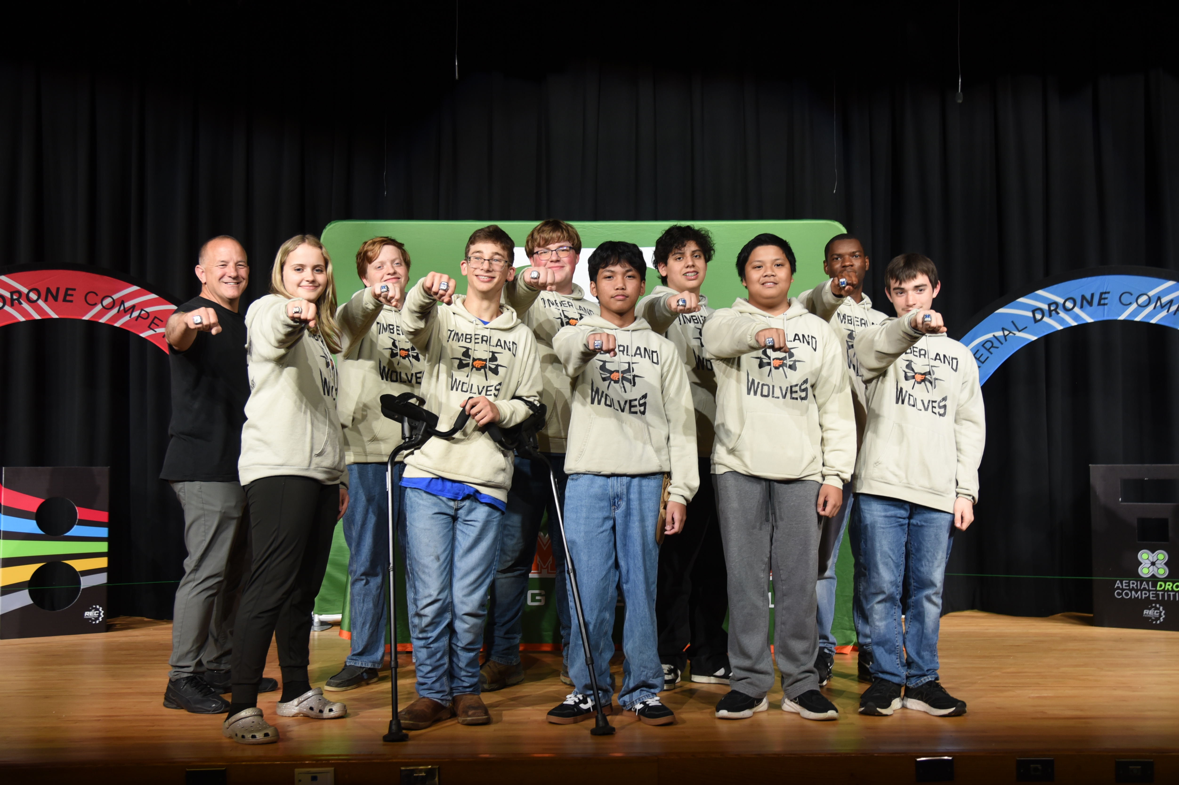 A group of people in matching tops and pants, standing on a stage, posing with hand signs.