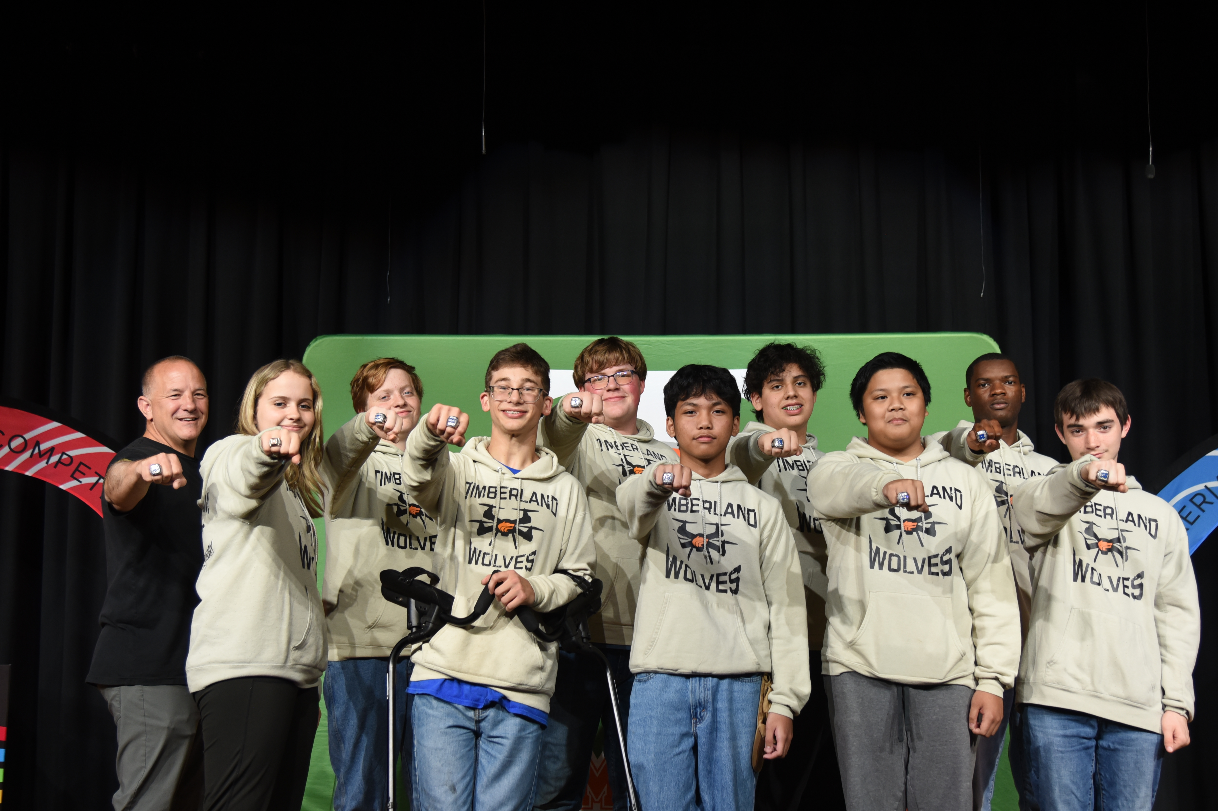 Group of people in matching sweatshirts pose for a photo in front of a green backdrop.