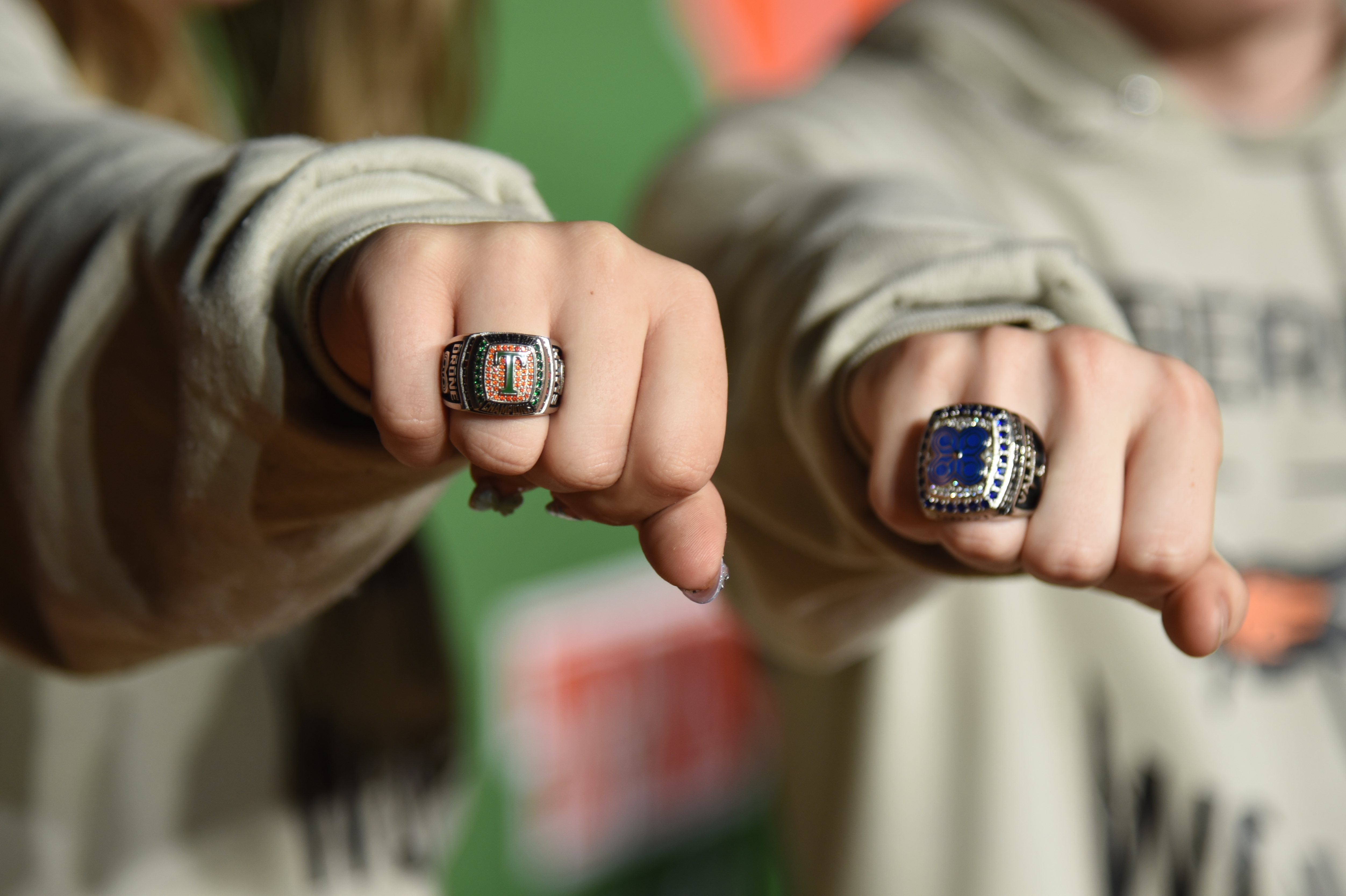Two people display rings on their index fingers; one ring has a blue stone, and the other has a square setting.