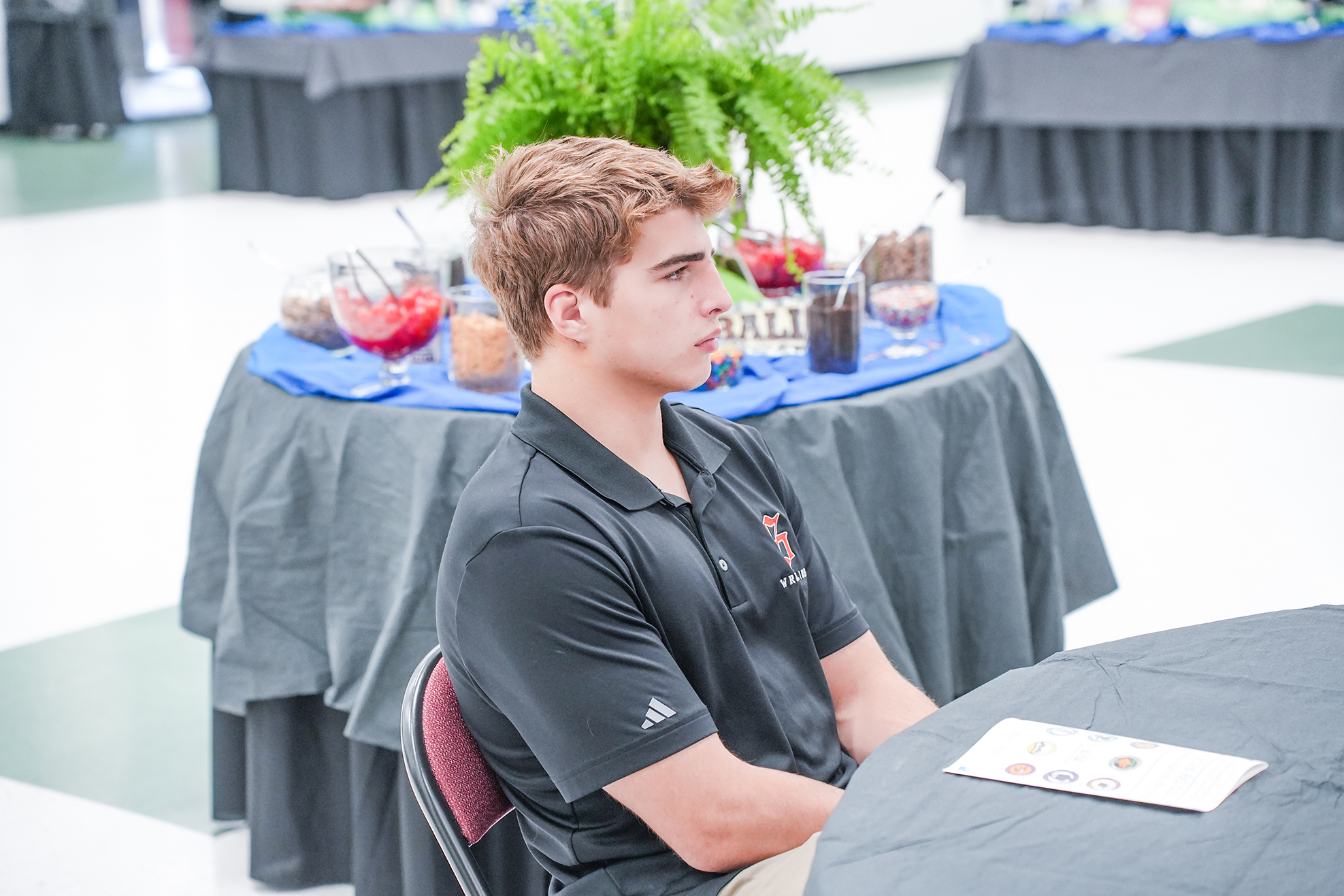 Man with light brown hair sits at table with blue tablecloth and menu in front of him.
